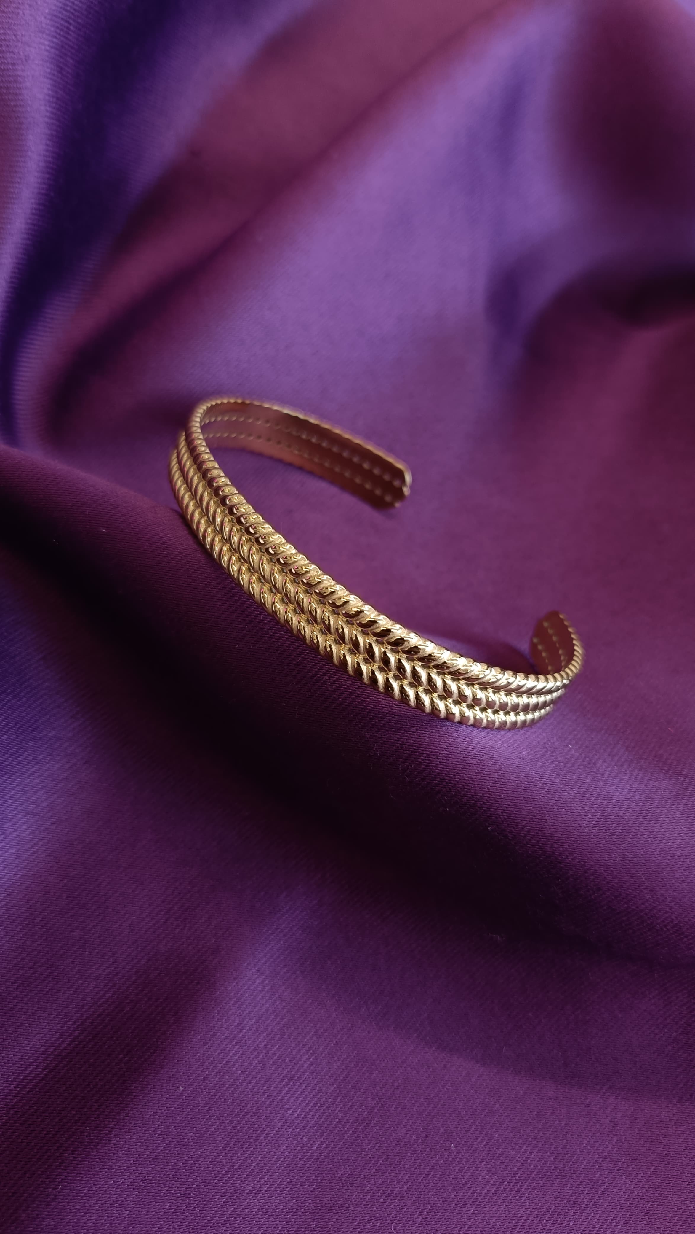 Gold Triple-Row Wheat Grain Textured Open Cuff Bracelet flat lay on purple fabric