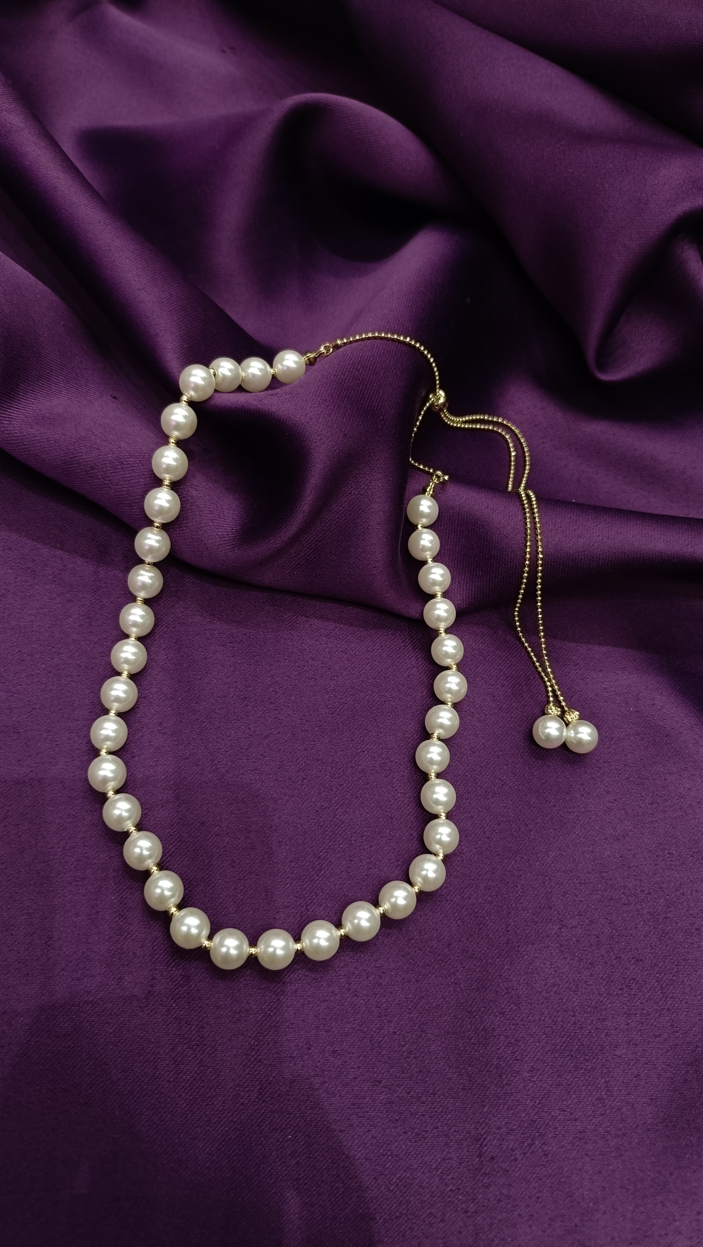 Gold Graduated Pearl Necklace with Adjustable Slider Closure full length flat lay on purple fabric showing slider closure