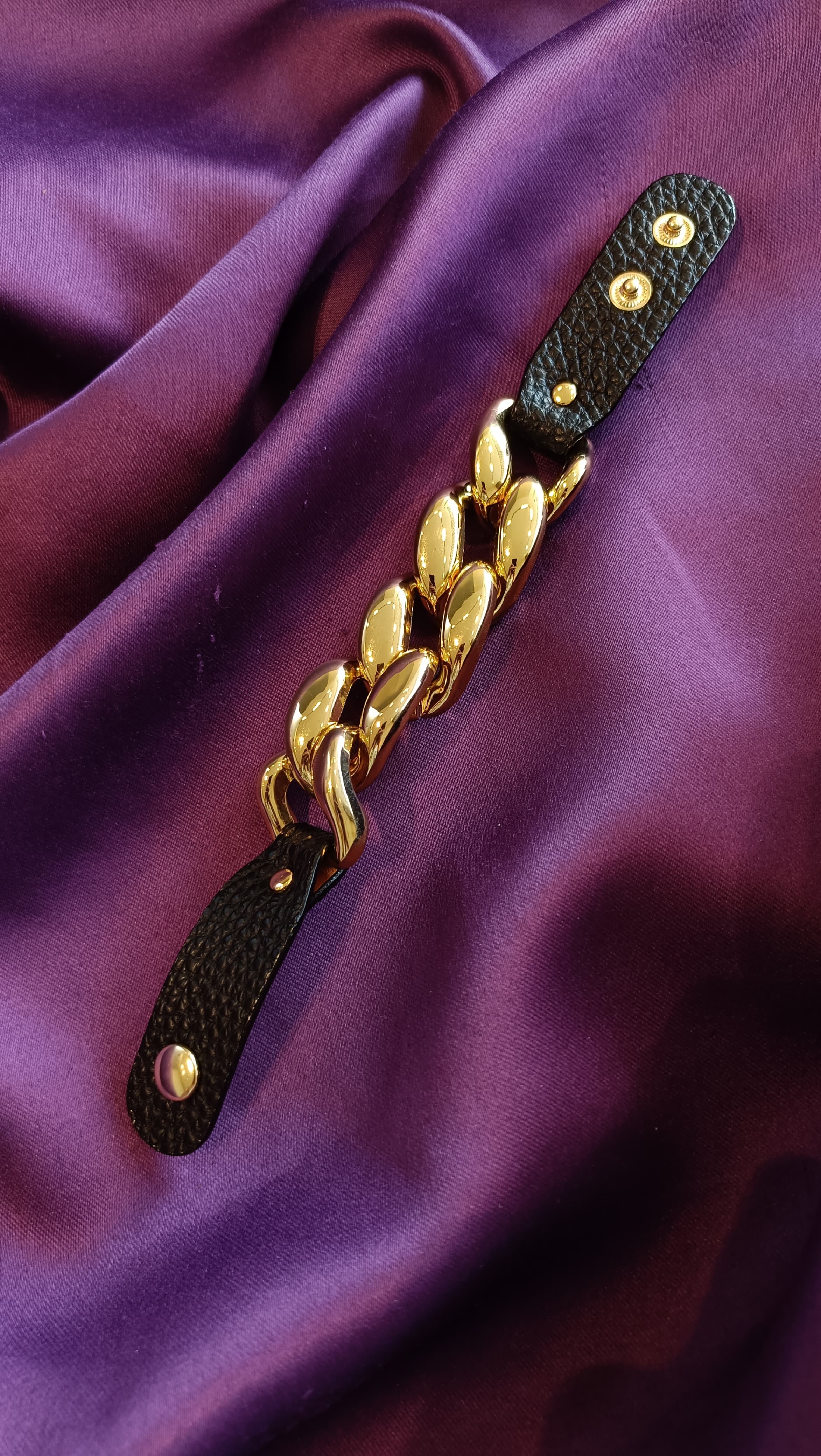 Gold Chunky Curb Chain Black Leather Strap Bracelet flat lay on purple fabric