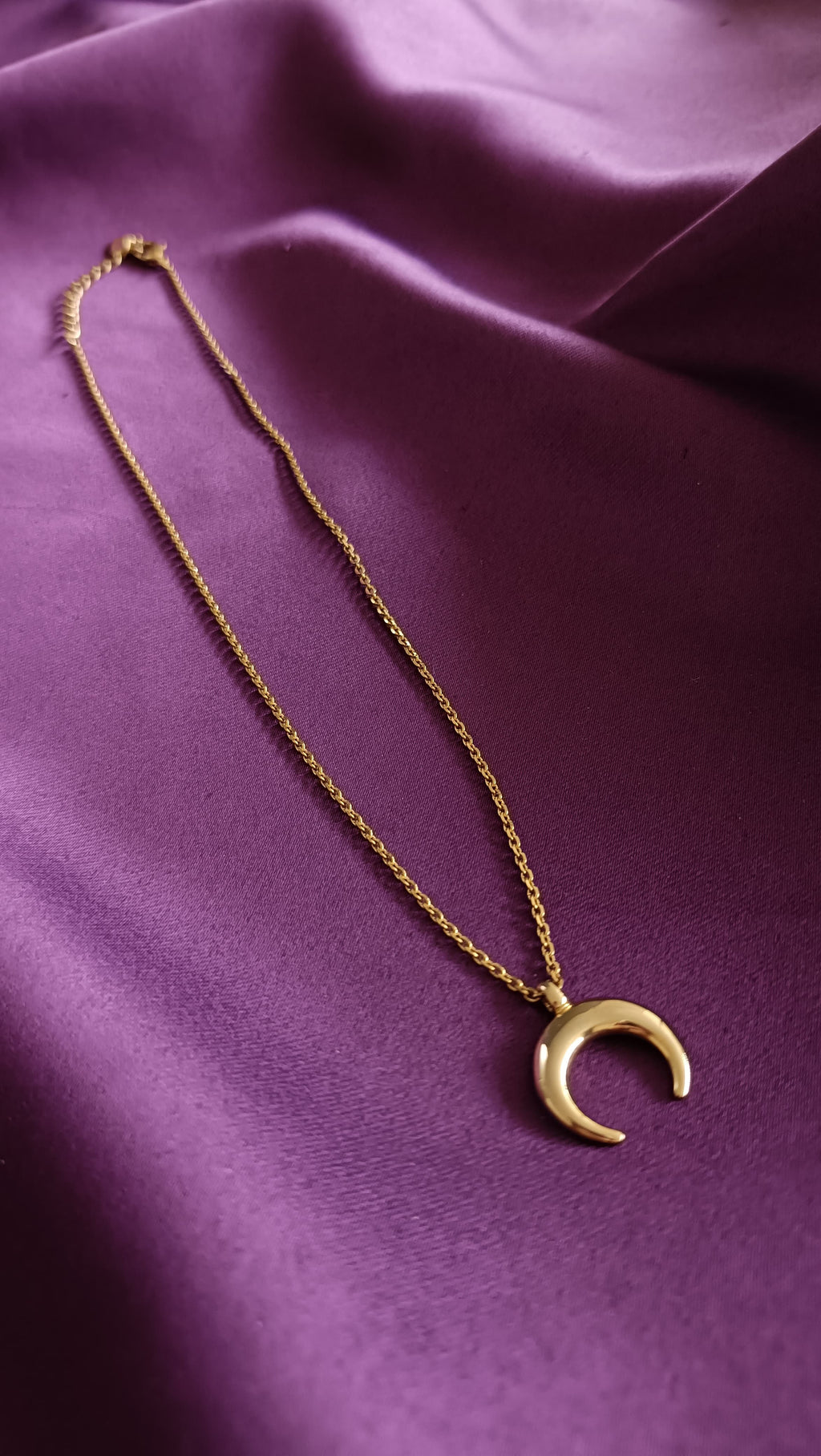 Gold Crescent Moon Pendant Necklace flat lay on purple fabric