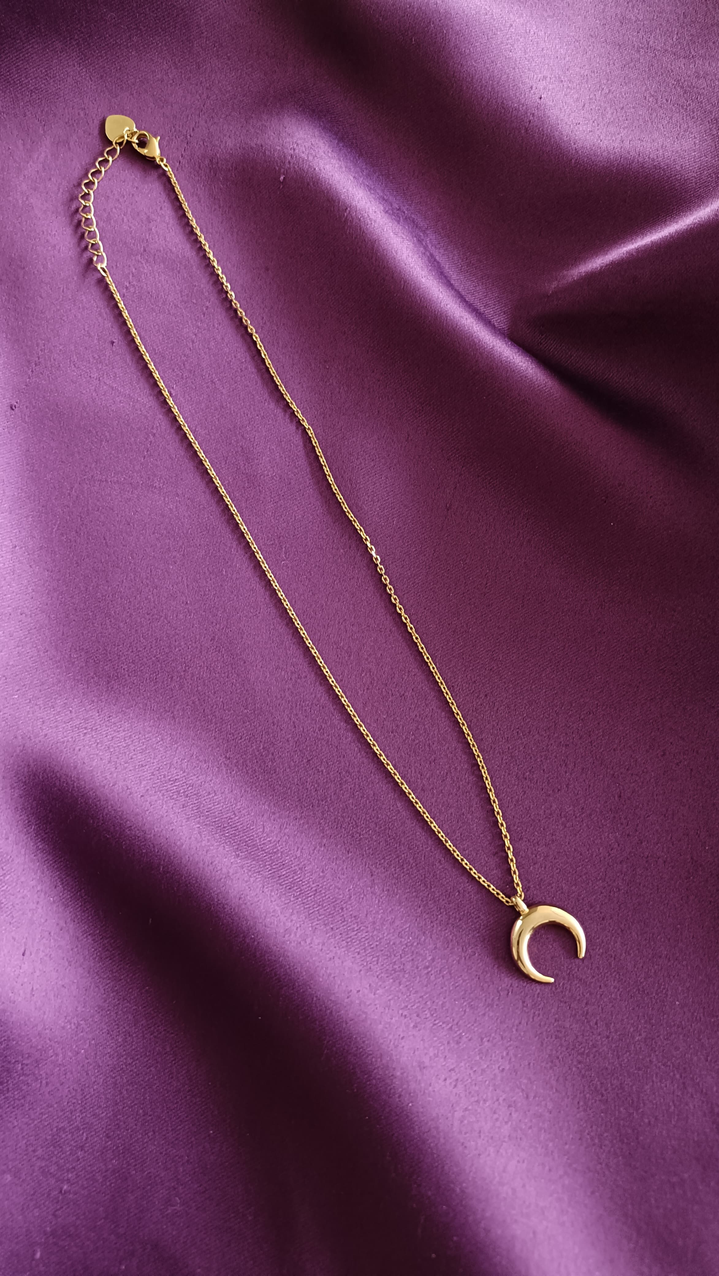 Gold Crescent Moon Pendant Necklace full length flat lay on purple fabric