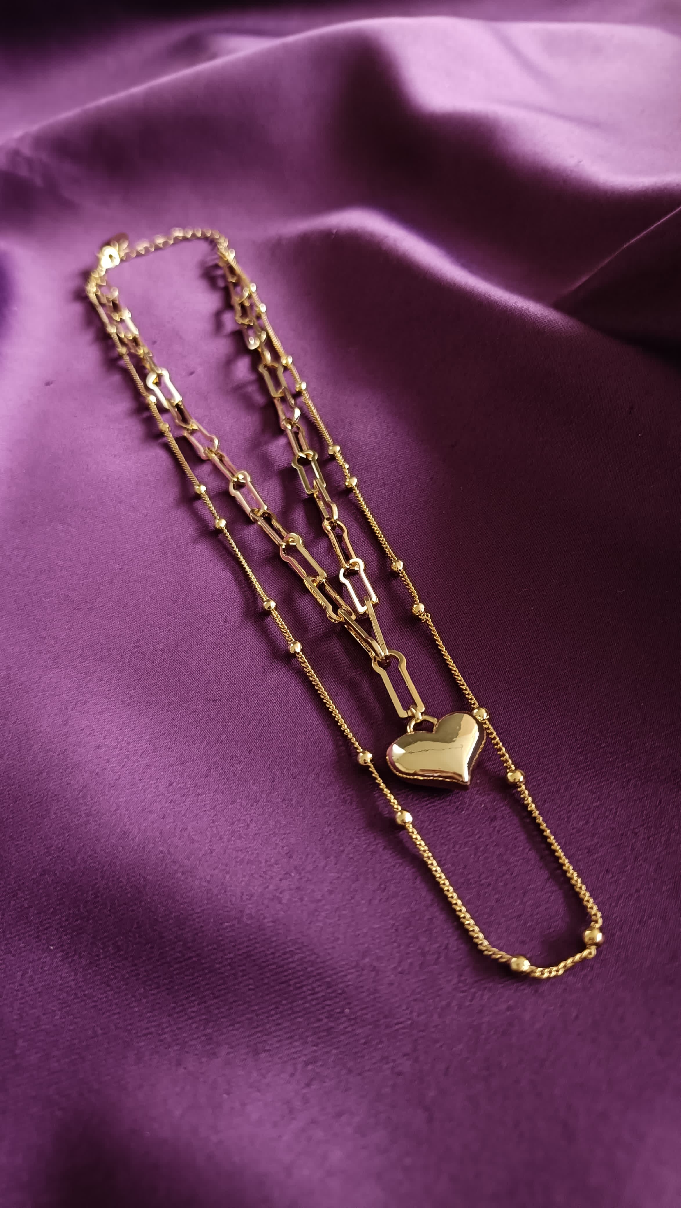 Gold Double-Layer Heart Pendant Necklace Set flat lay on purple fabric