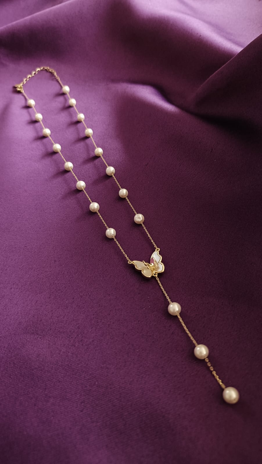 Gold Pearl Station Butterfly Lariat Necklace flat lay on purple fabric