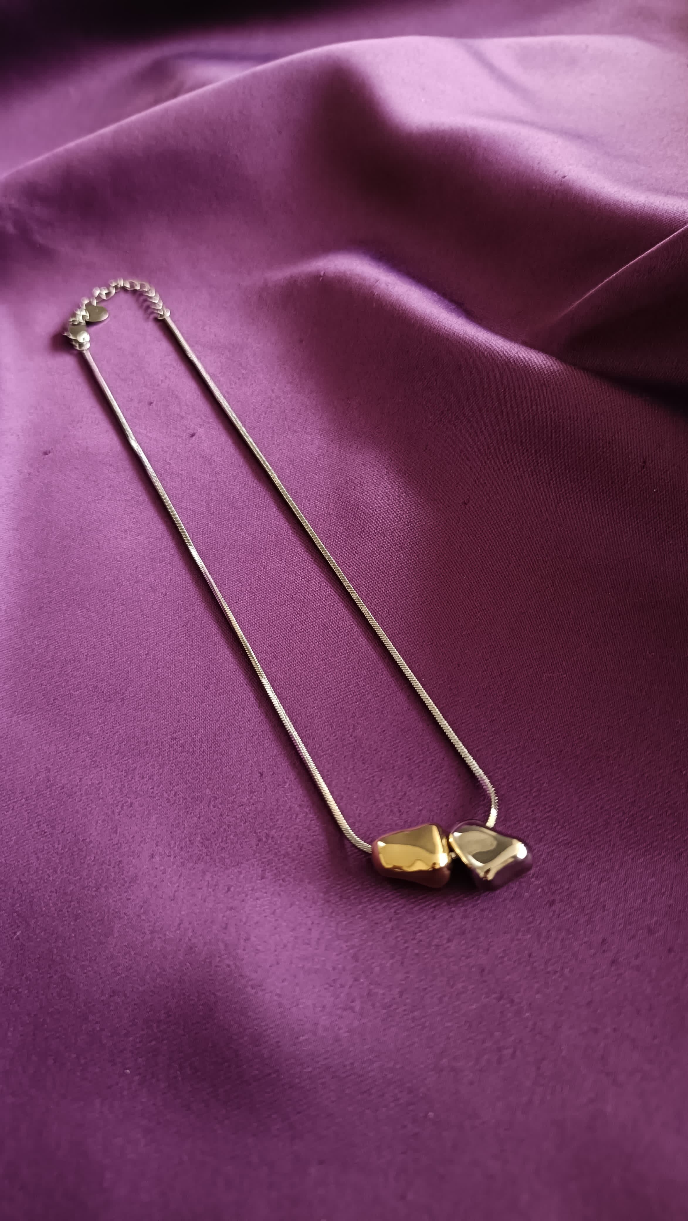 Bi-Tone Double Pebble Heart Necklace flat lay on purple fabric