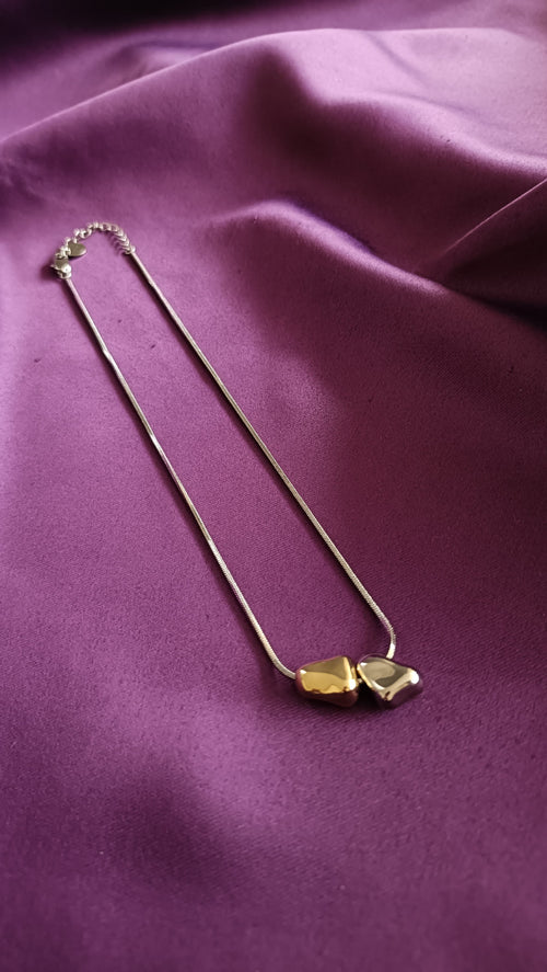 Bi-Tone Double Pebble Heart Necklace flat lay on purple fabric