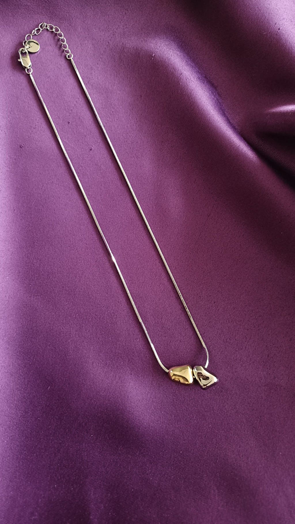 Bi-Tone Double Pebble Heart Necklace full length flat lay on purple fabric