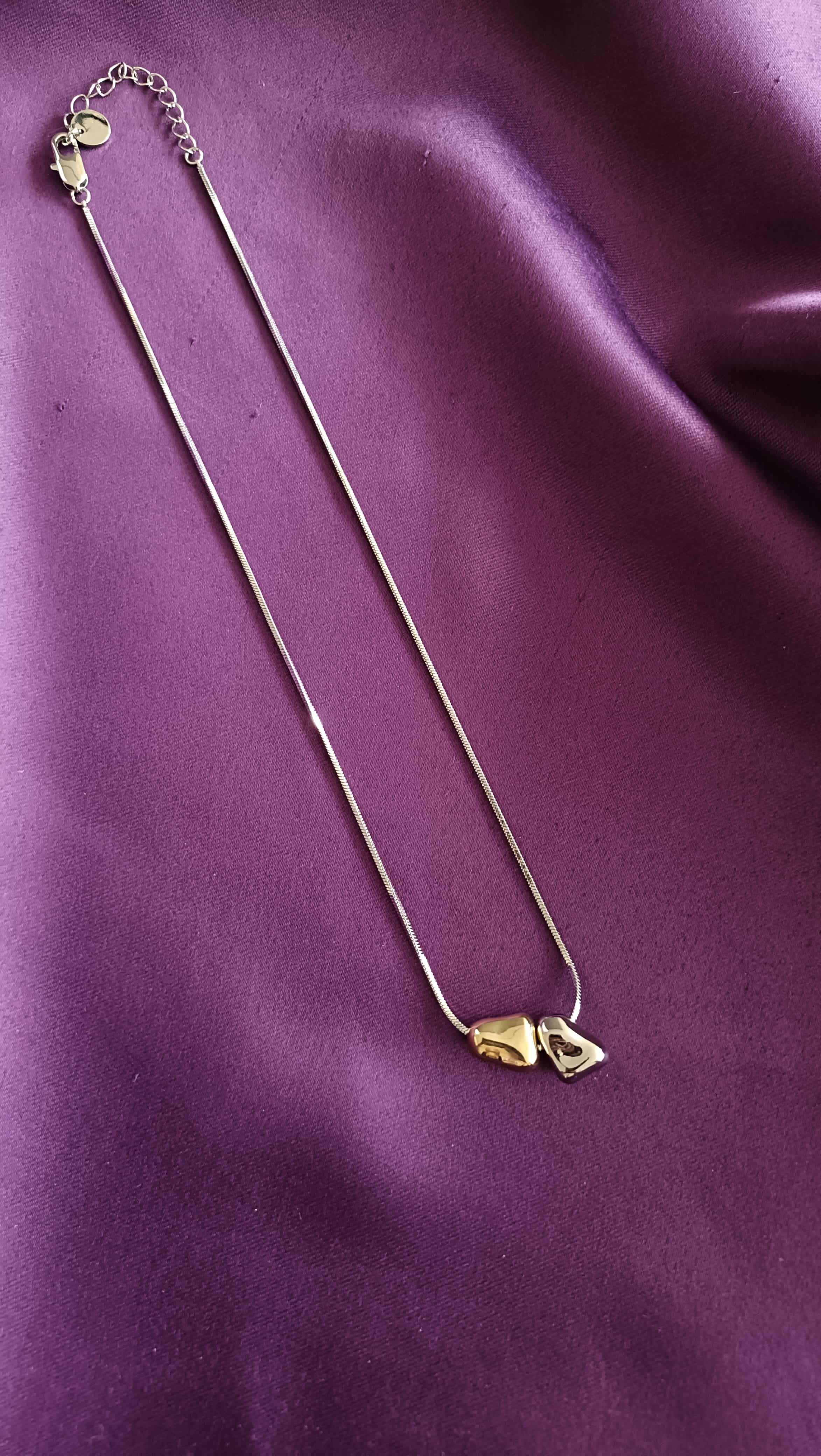 Bi-Tone Double Pebble Heart Necklace full length flat lay on purple fabric