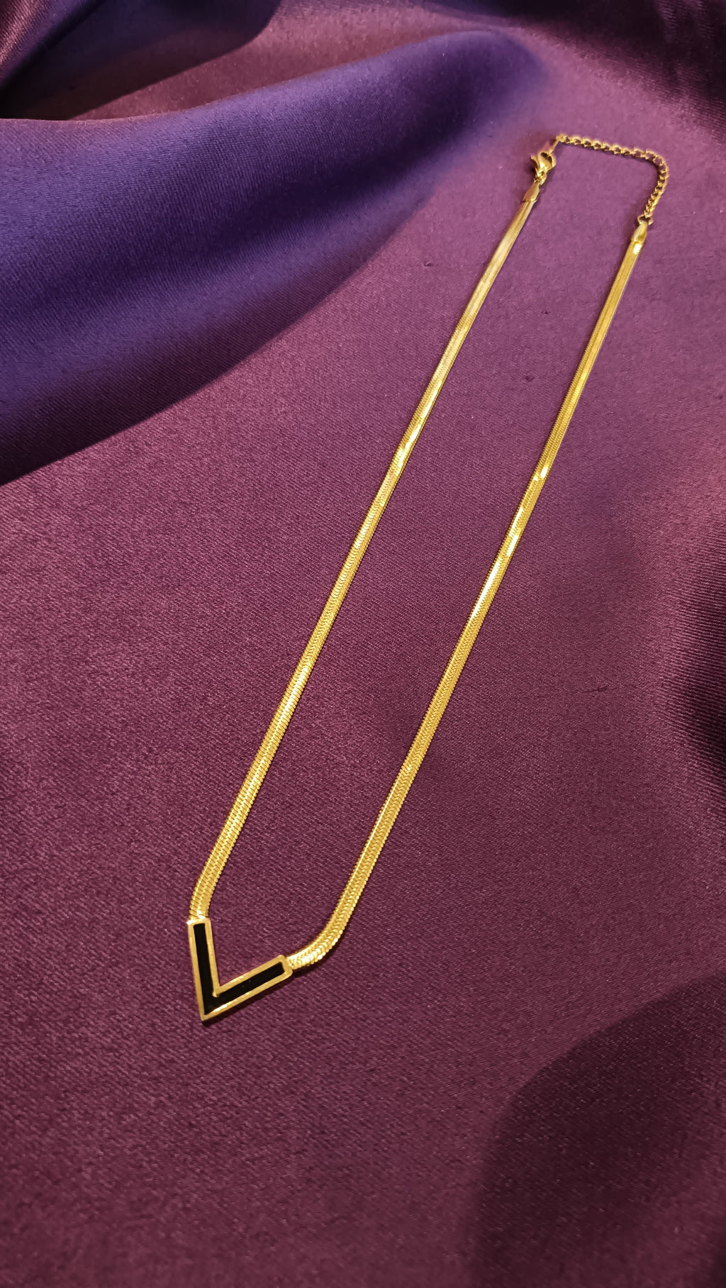 Gold Black Enamel V-Chevron Herringbone Chain Necklace V-pendant close-up flat lay on purple fabric