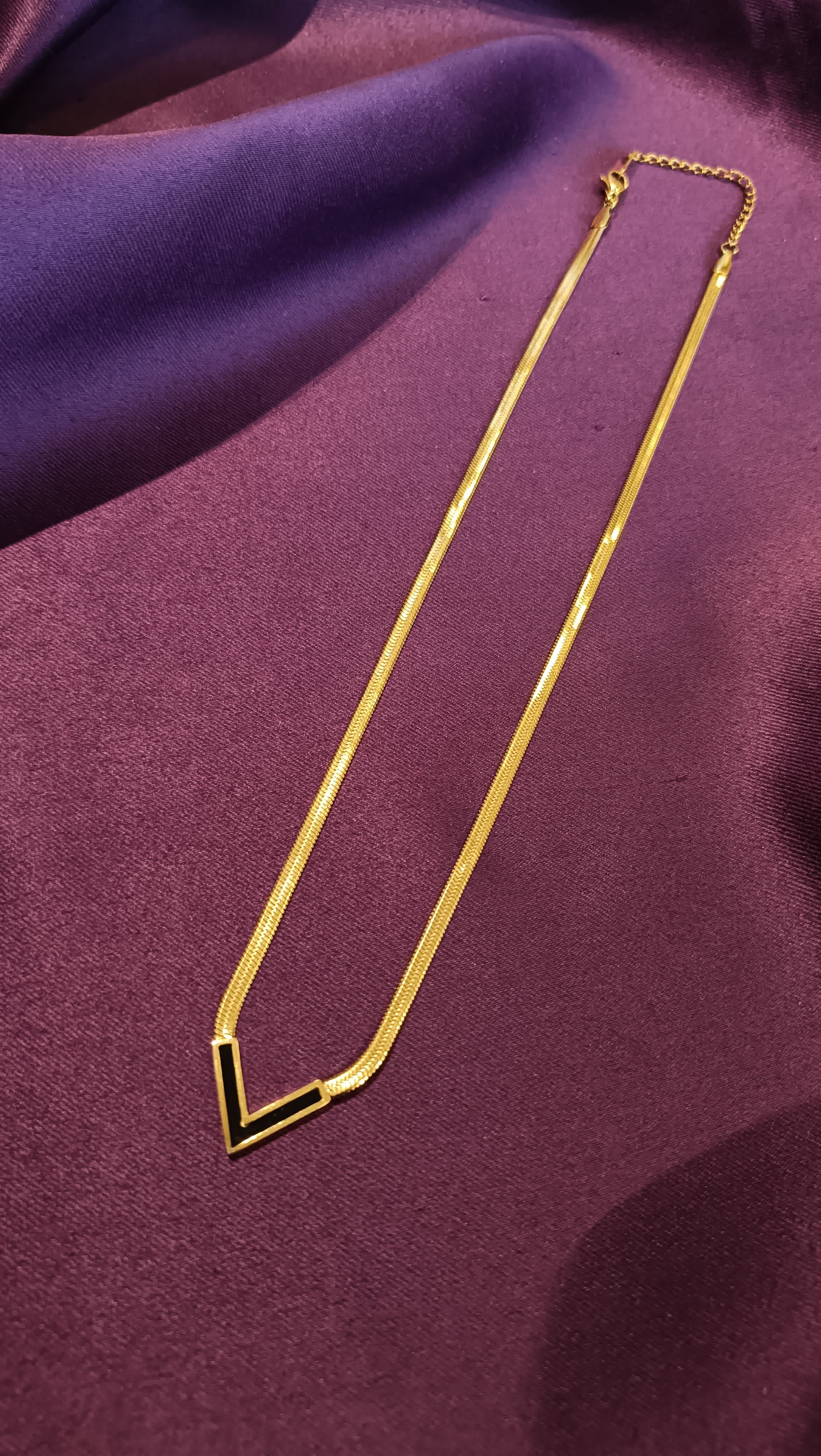 Gold Black Enamel V-Chevron Herringbone Chain Necklace V-pendant close-up flat lay on purple fabric
