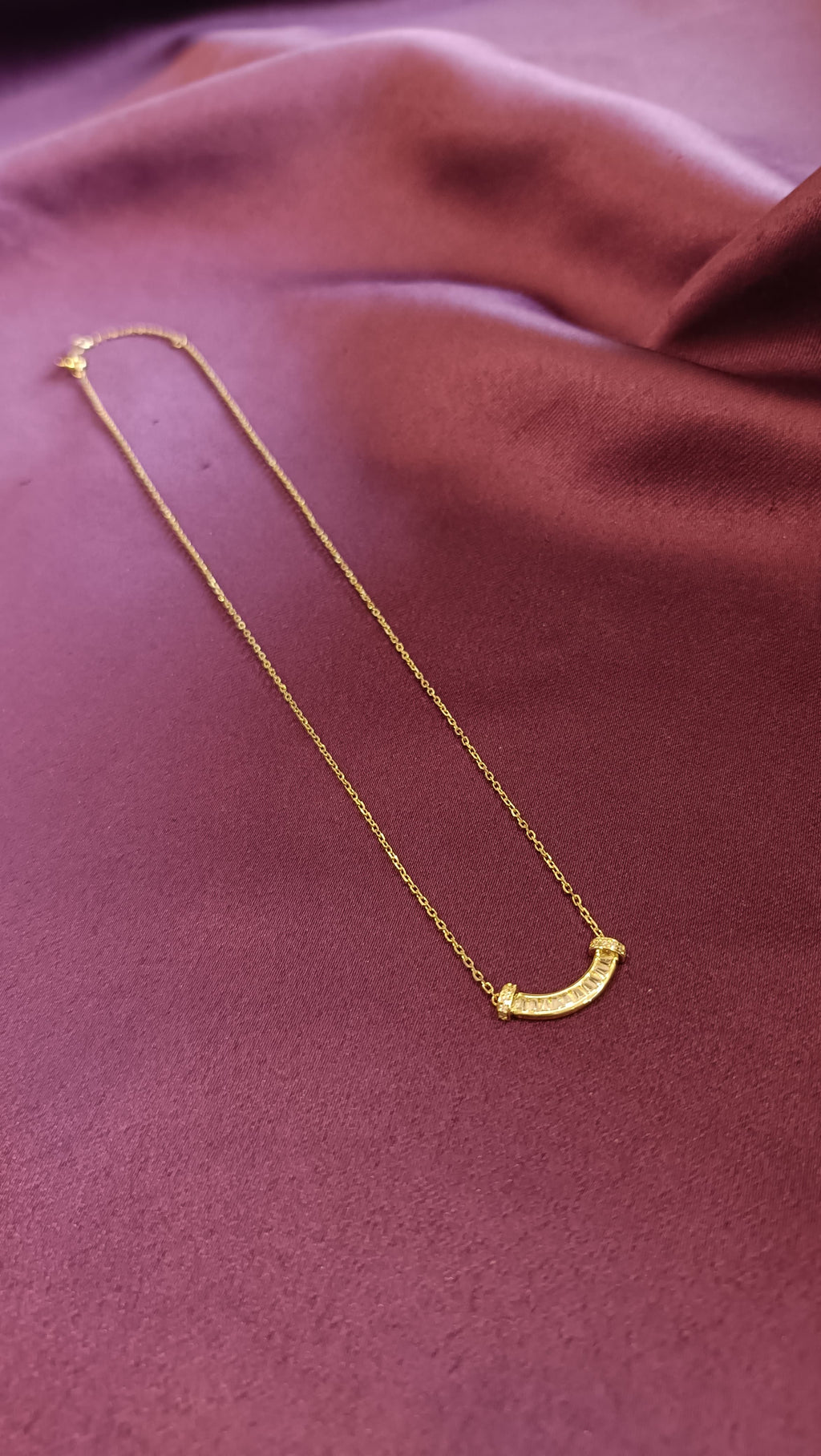 Gold Curved Baguette Bar Necklace close-up flat lay on purple fabric