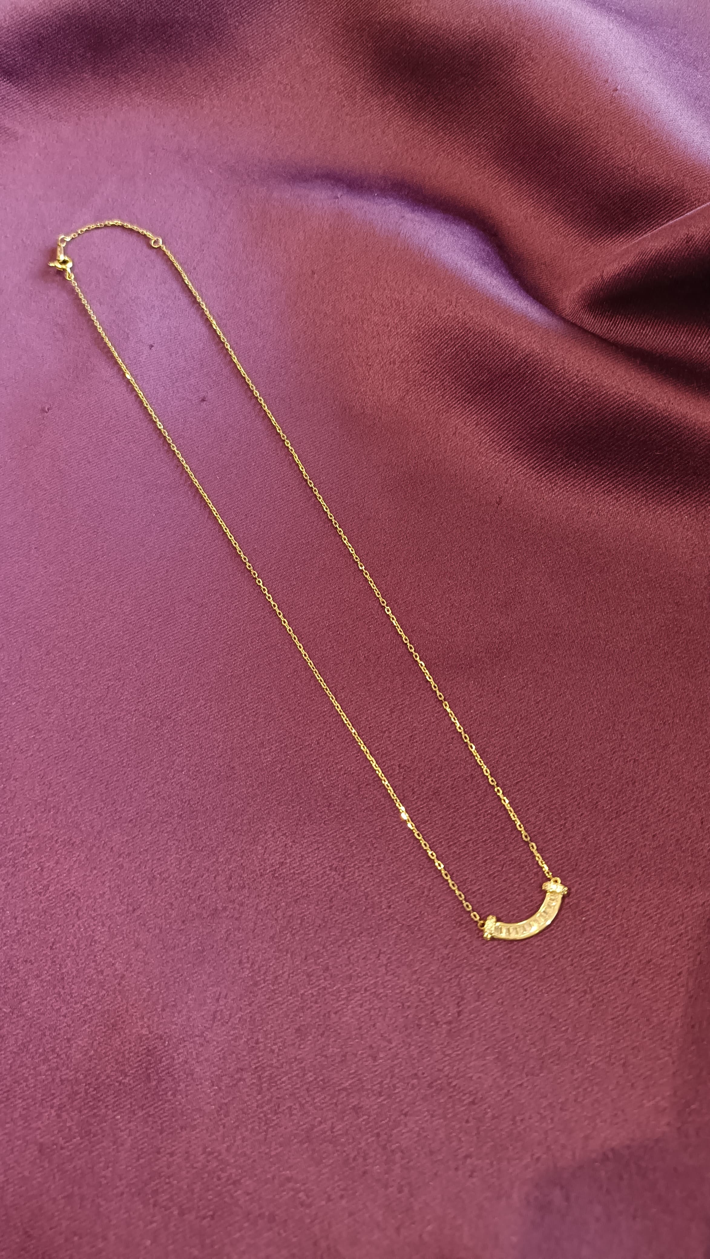 Gold Curved Baguette Bar Necklace flat lay on purple fabric
