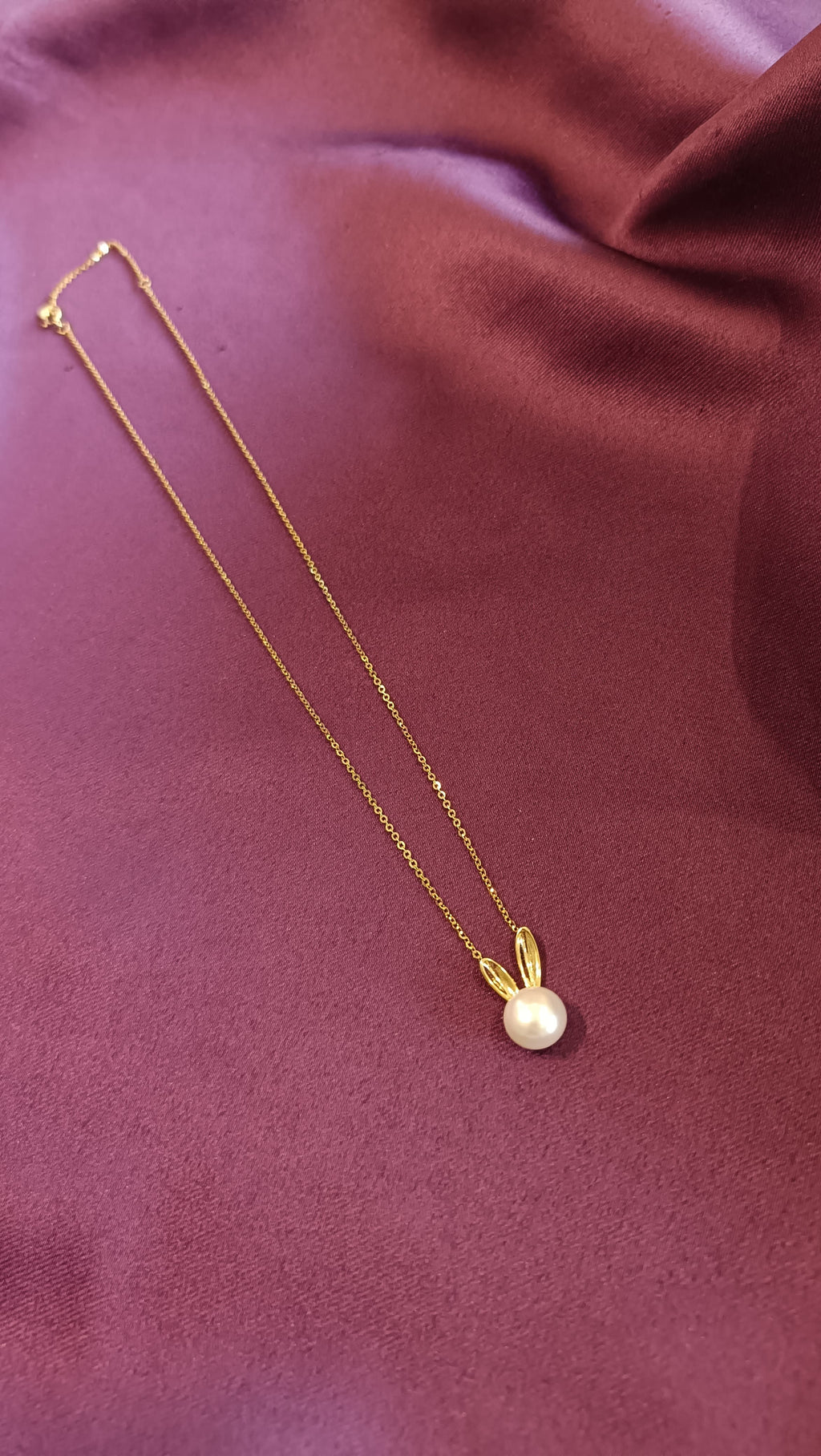 Gold Pearl Bunny Pendant Necklace flat lay on purple fabric