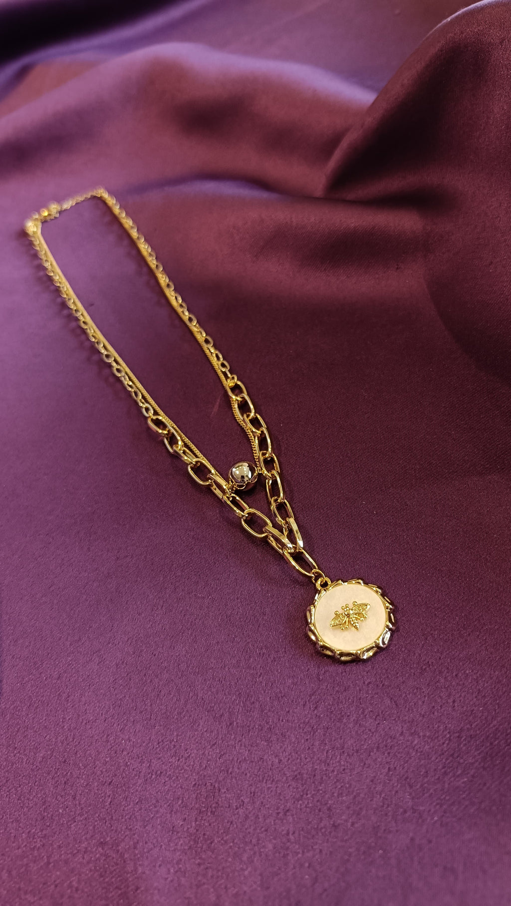 Gold Double-Layer Paperclip Chain Bee Medallion Necklace flat lay on purple fabric