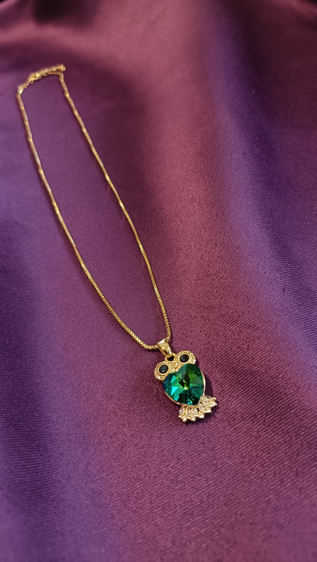 Gold Emerald Crystal Owl Pendant Box Chain Necklace close-up flat lay on purple fabric showing owl pendant detail with pavé eyes and wings
