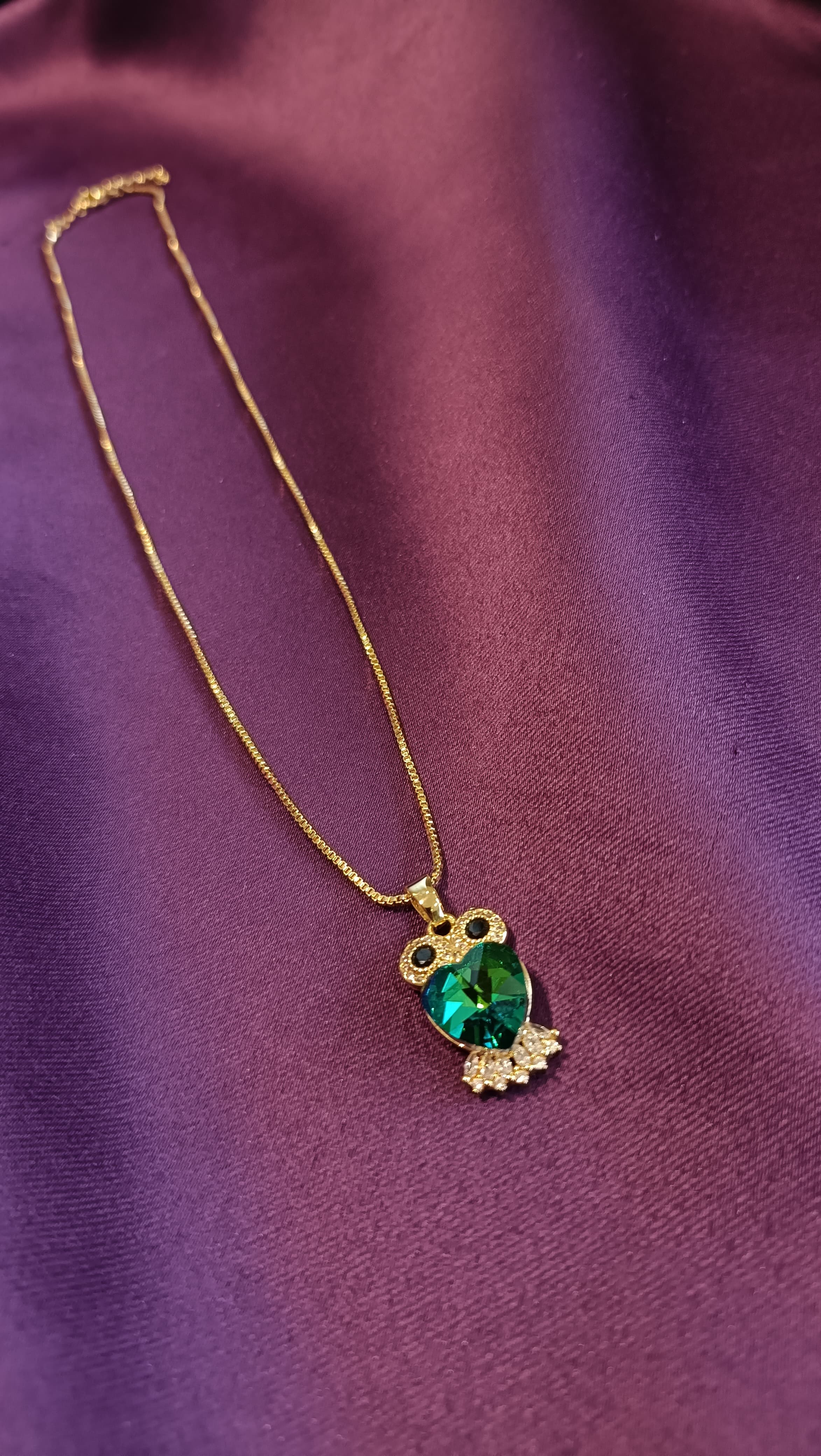 Gold Emerald Crystal Owl Pendant Box Chain Necklace close-up flat lay on purple fabric showing owl pendant detail with pavé eyes and wings