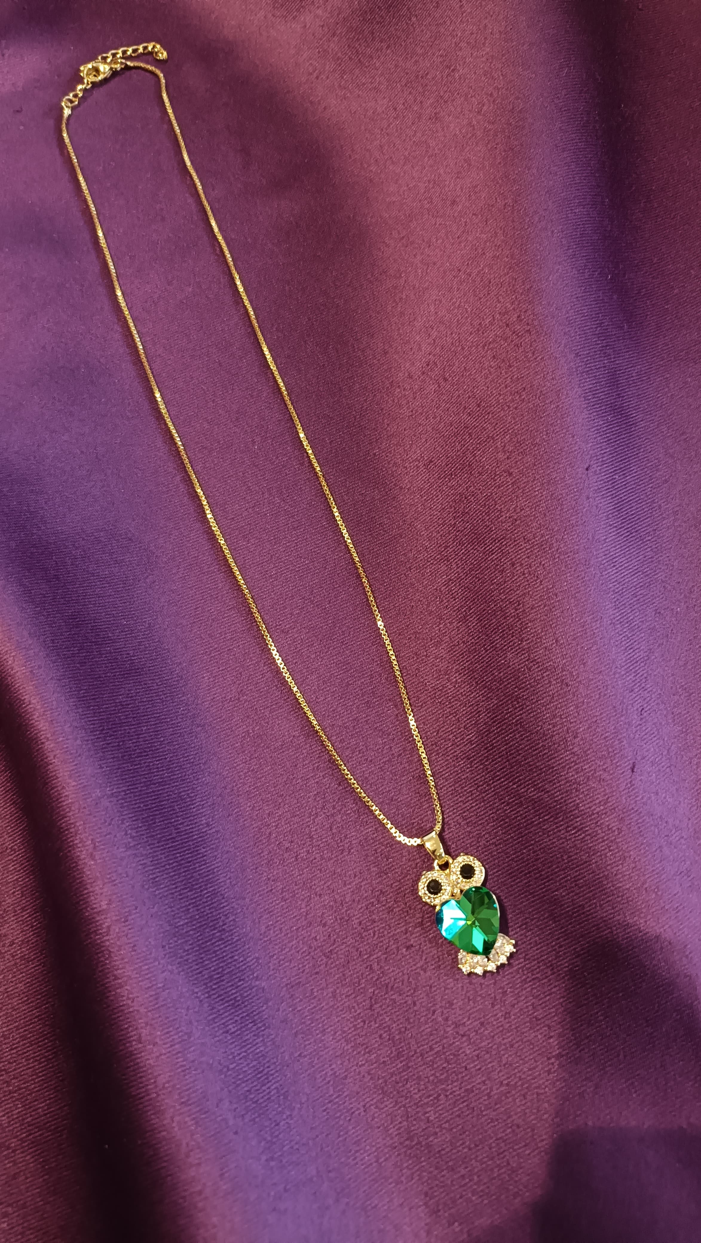Gold Emerald Crystal Owl Pendant Box Chain Necklace full length flat lay on purple fabric showing lobster clasp and extender