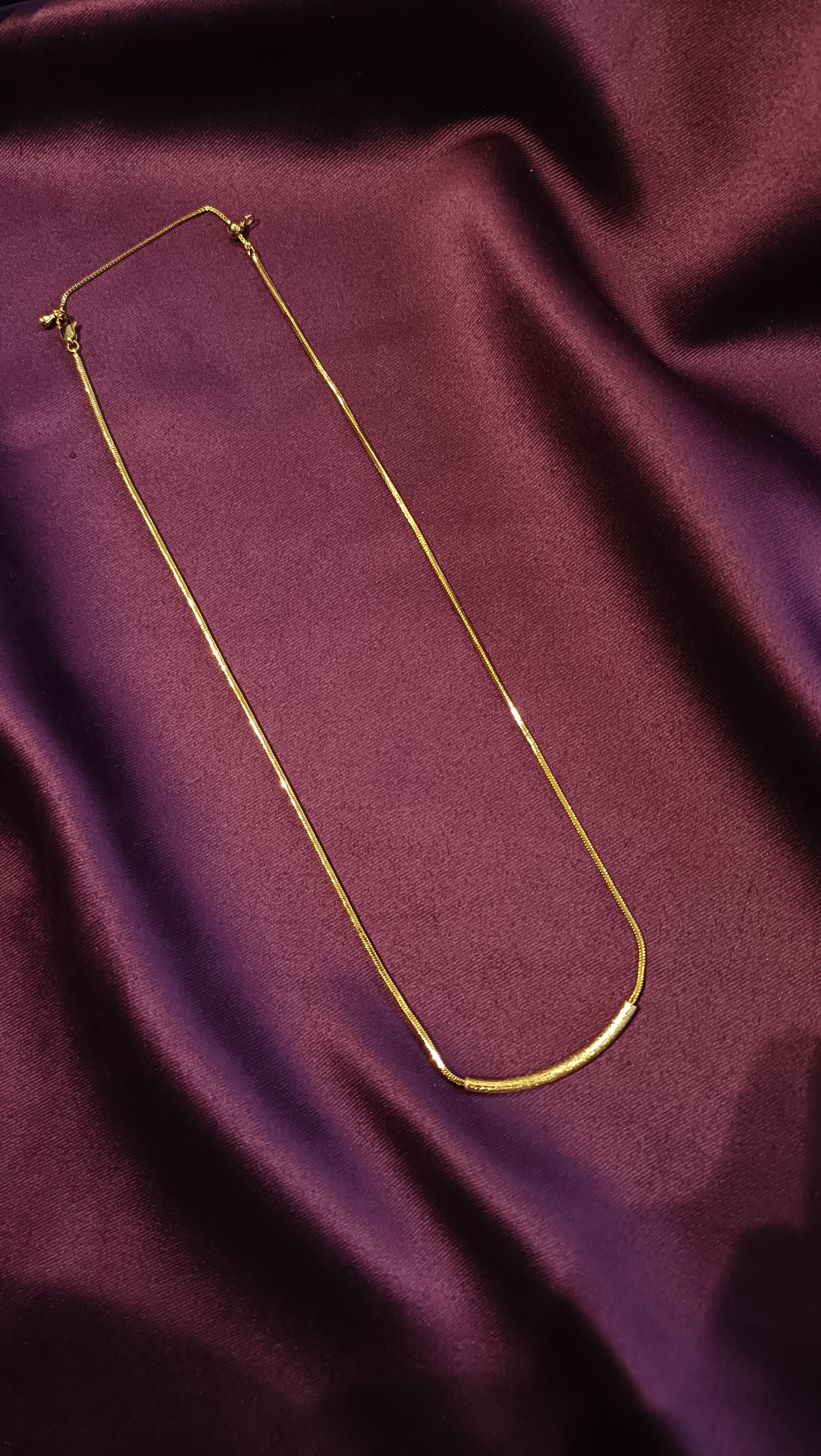 Gold Textured Curved Bar Necklace flat lay on purple fabric