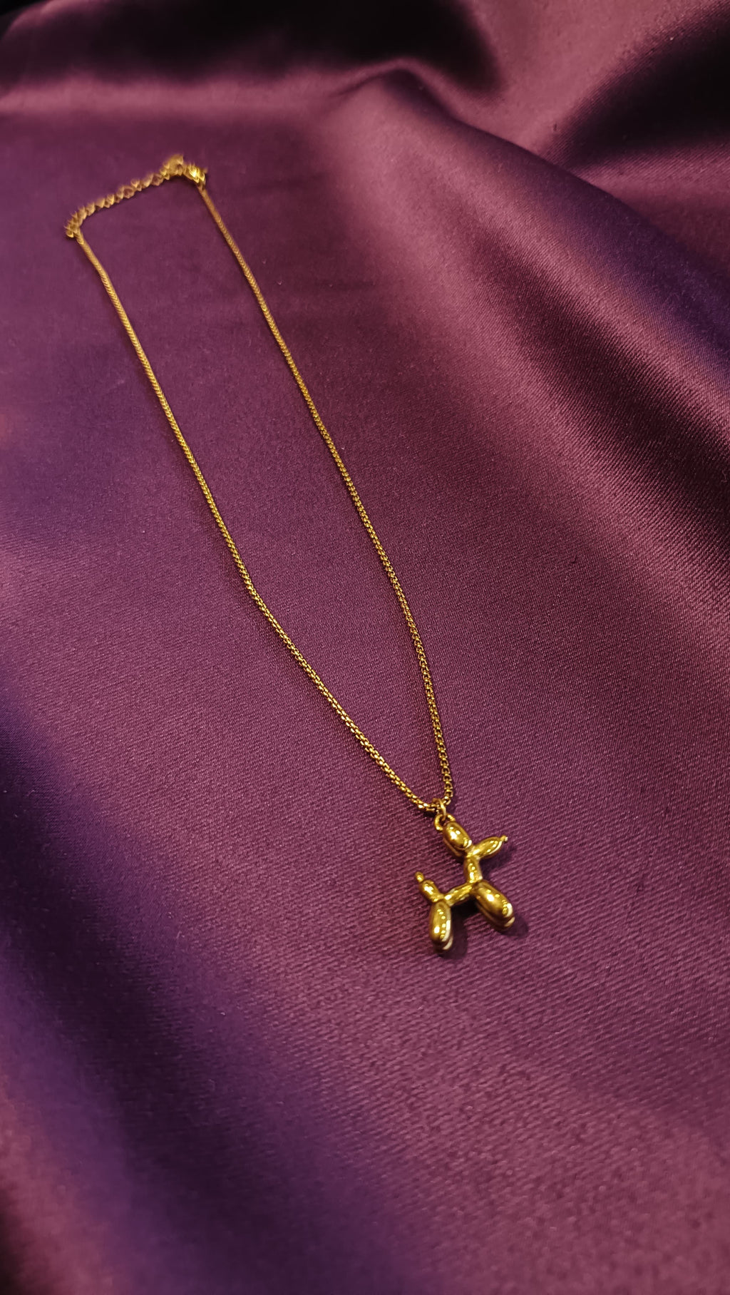 Gold Balloon Dog Pendant Necklace flat lay on purple fabric