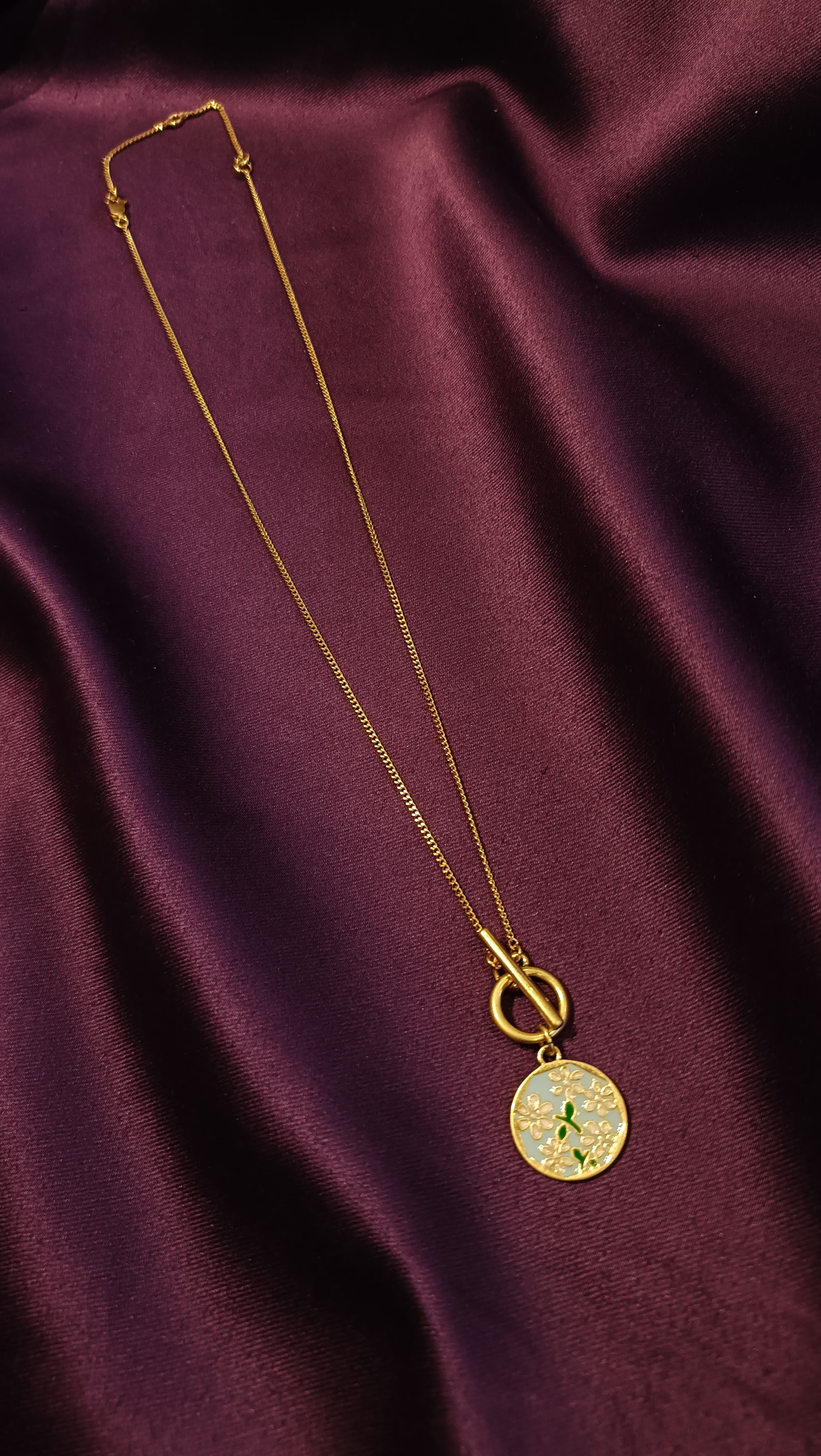 Gold Sky Blue Floral Enamel Coin Pendant Necklace flat lay on purple fabric