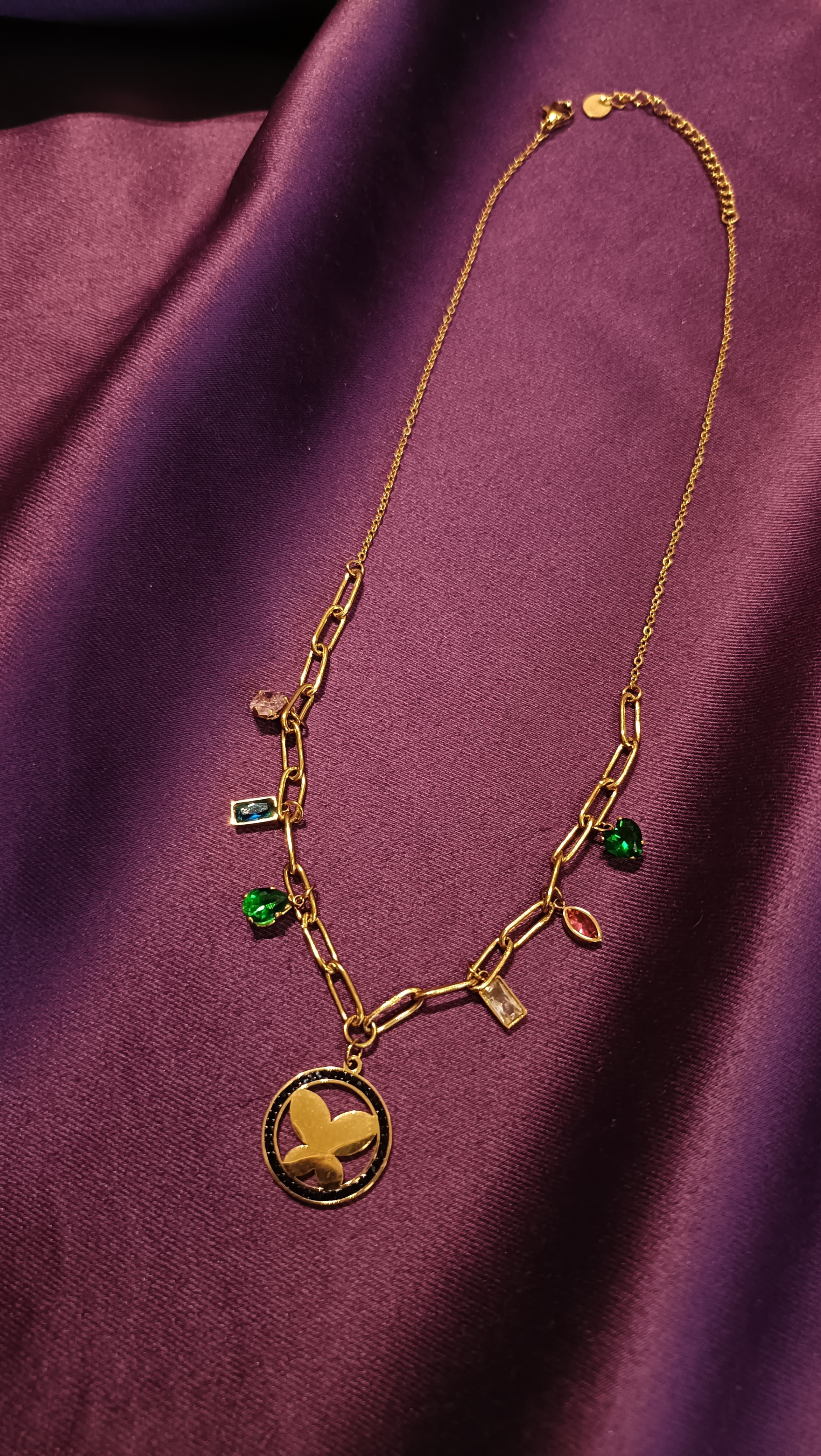 Gold Multi-Crystal Charm Paperclip Chain Butterfly Medallion Necklace full length flat lay on purple fabric