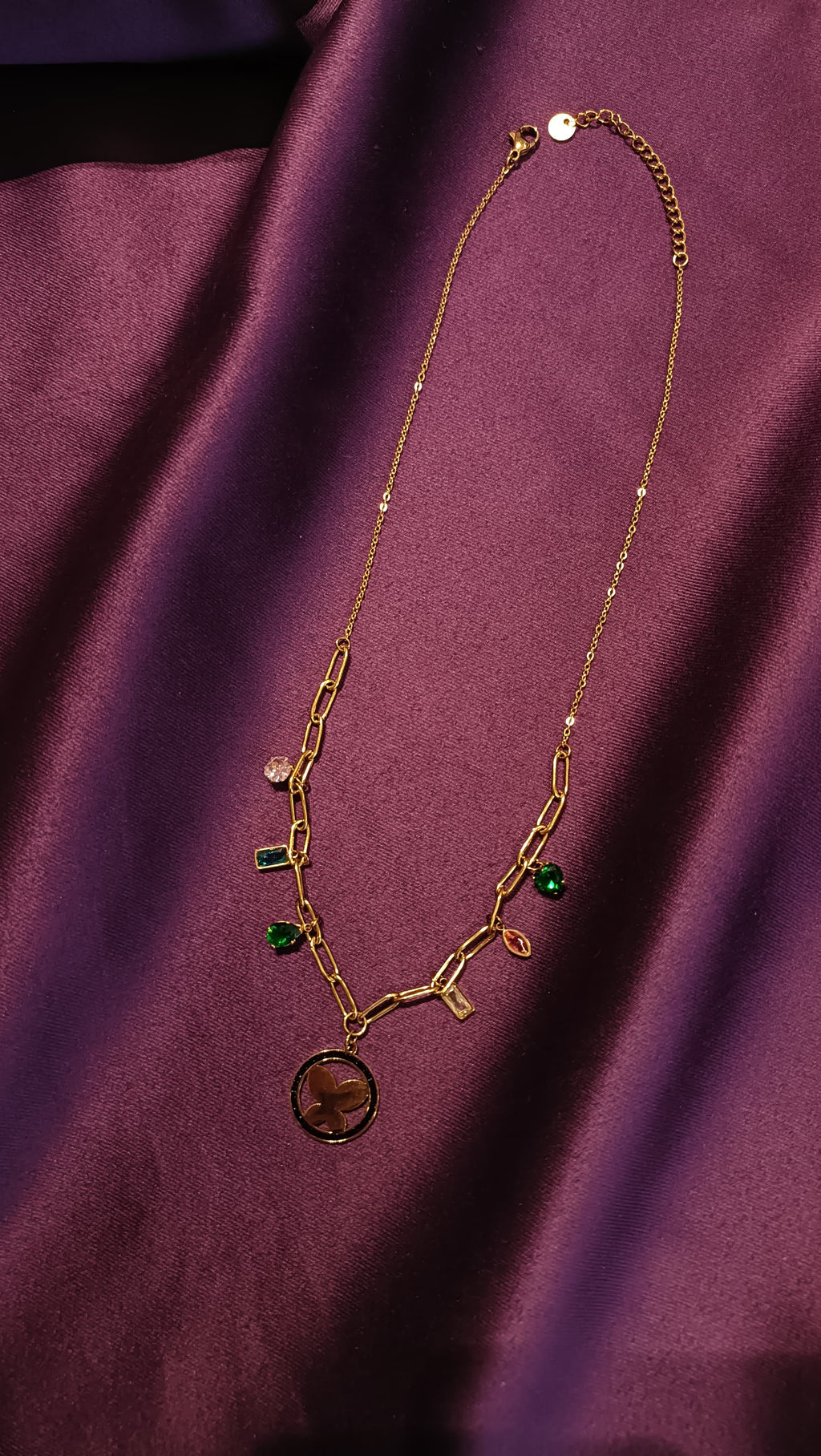 Gold Multi-Crystal Charm Paperclip Chain Butterfly Medallion Necklace flat lay on purple fabric
