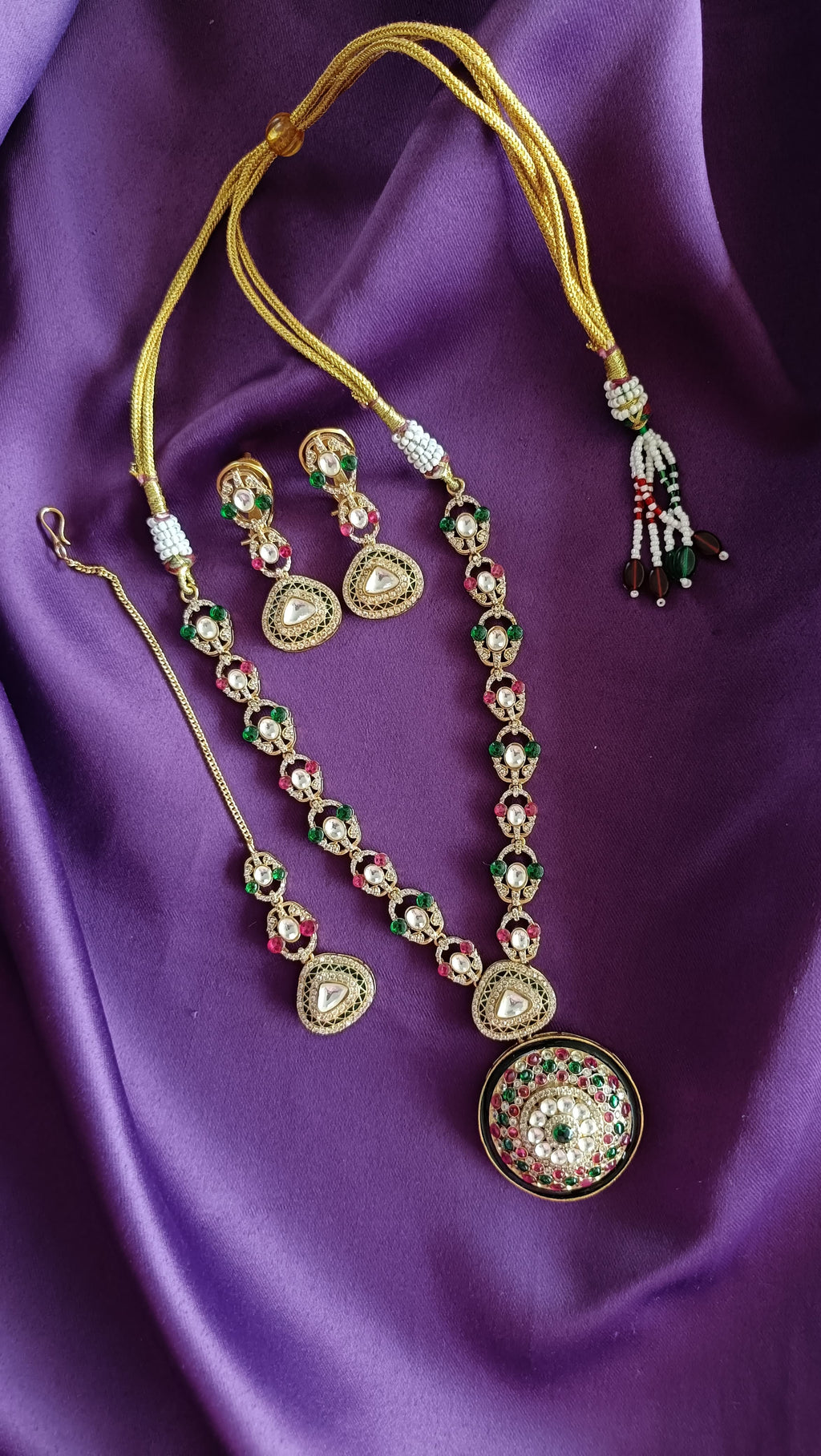 Gold Kundan Polki Ruby & Emerald Long Necklace with domed pendant close-up flat lay on purple fabric