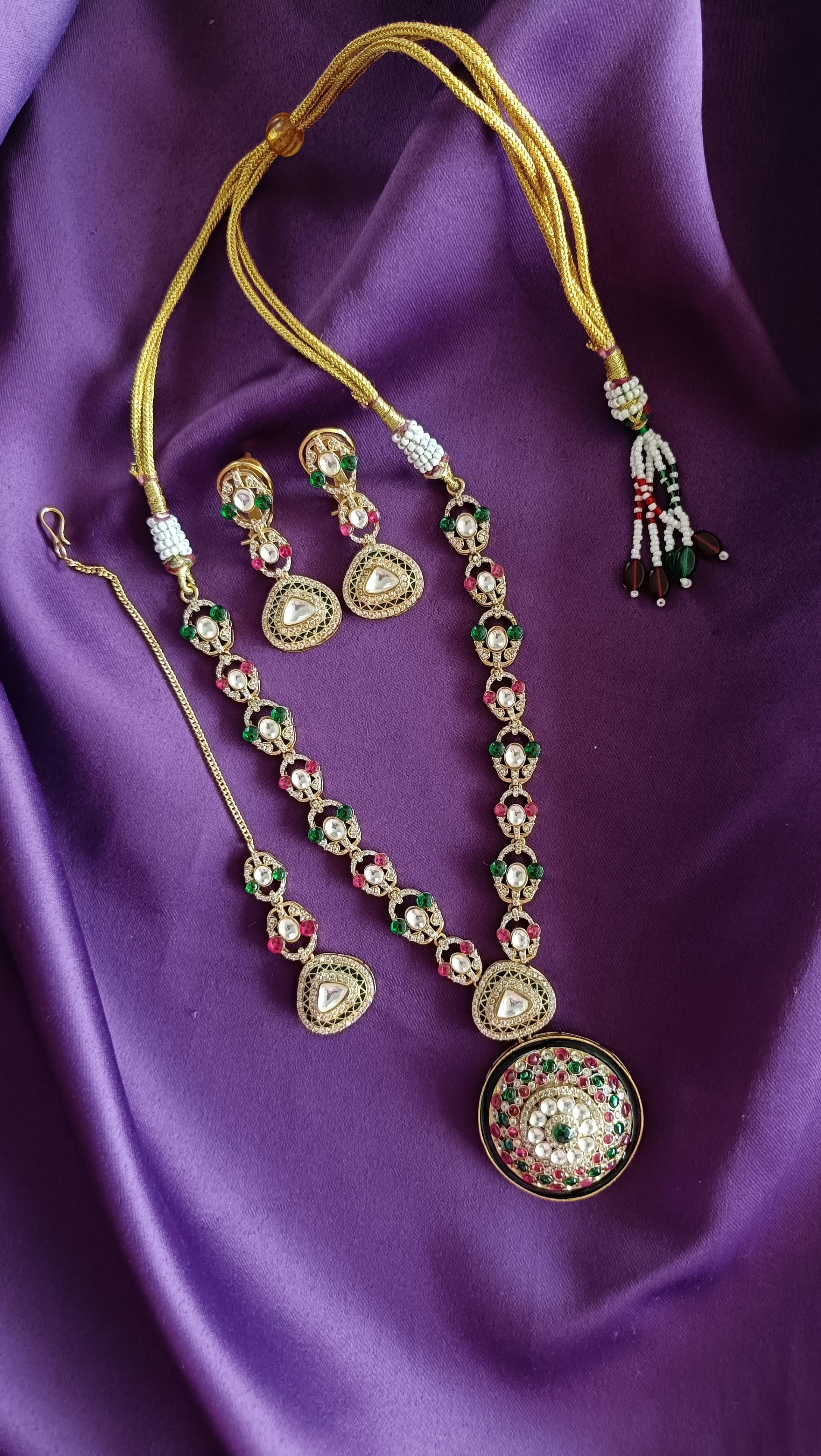 Gold Kundan Polki Ruby & Emerald Long Necklace with domed pendant close-up flat lay on purple fabric