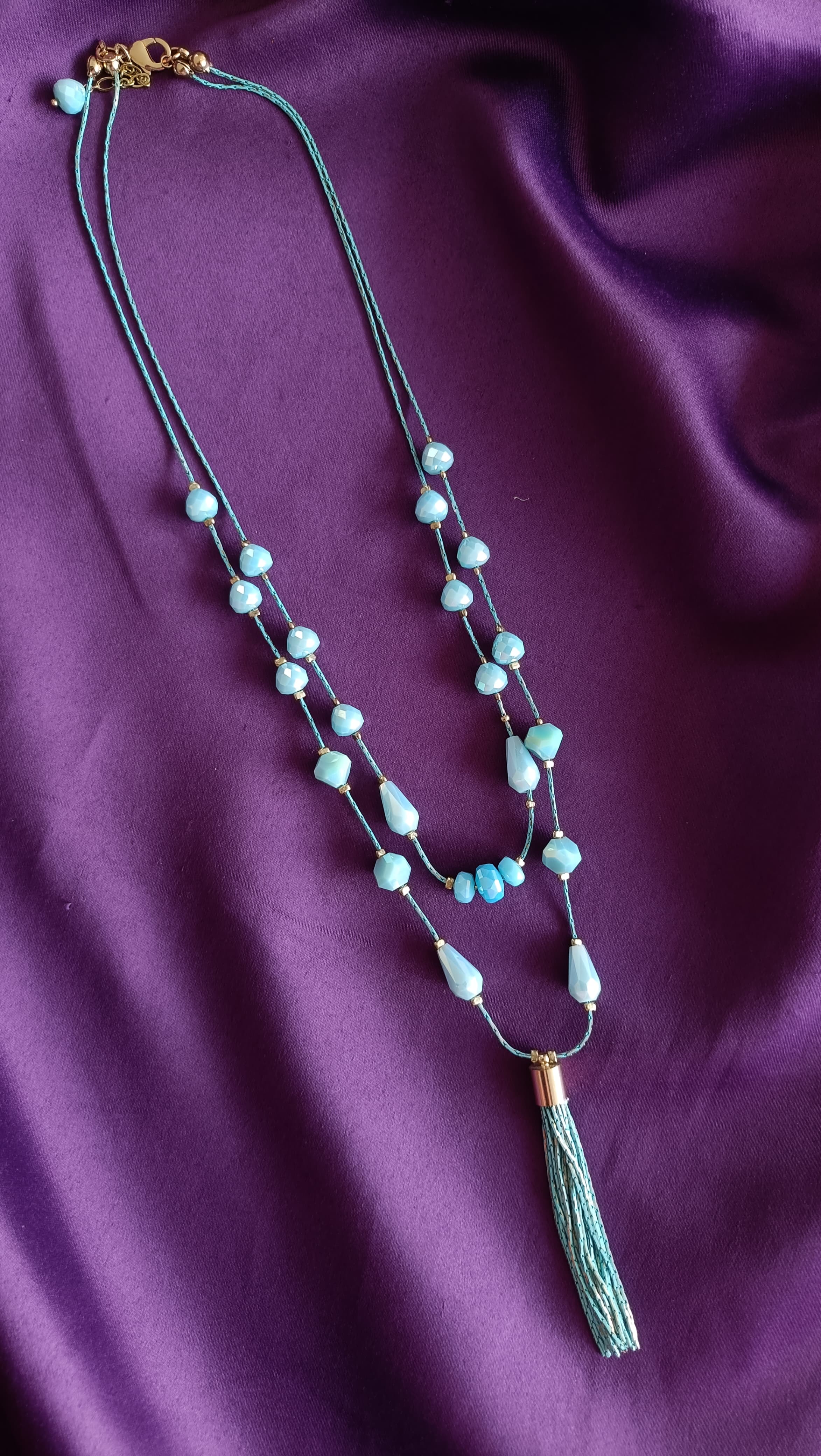 Turquoise Double-Strand Tumbled Bead & Teardrop Long Tassel Necklace full length flat lay on purple fabric showing lobster clasp and tassel