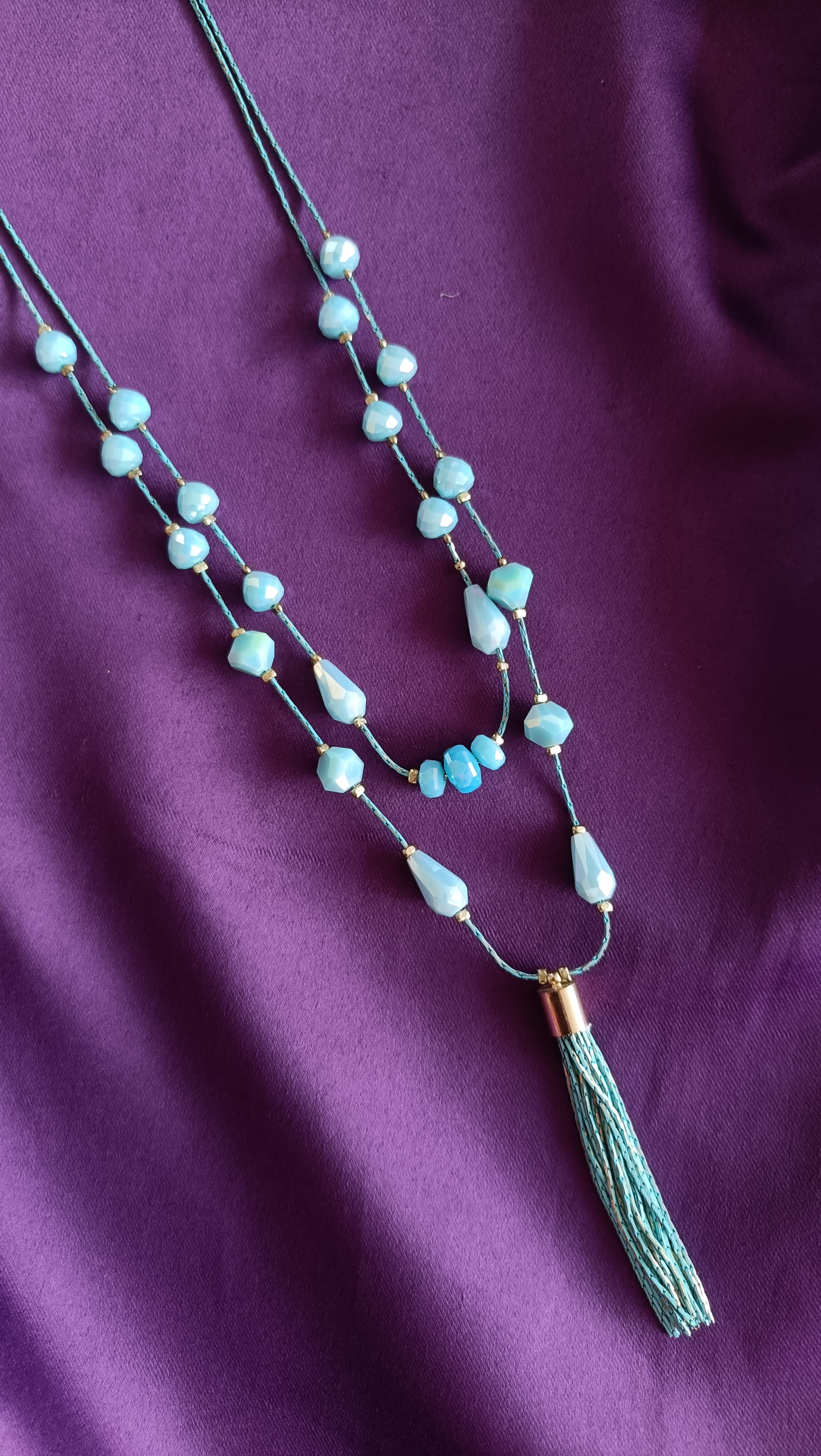 Turquoise Double-Strand Tumbled Bead & Teardrop Long Tassel Necklace centre detail flat lay on purple fabric showing gold cap and tassel drop