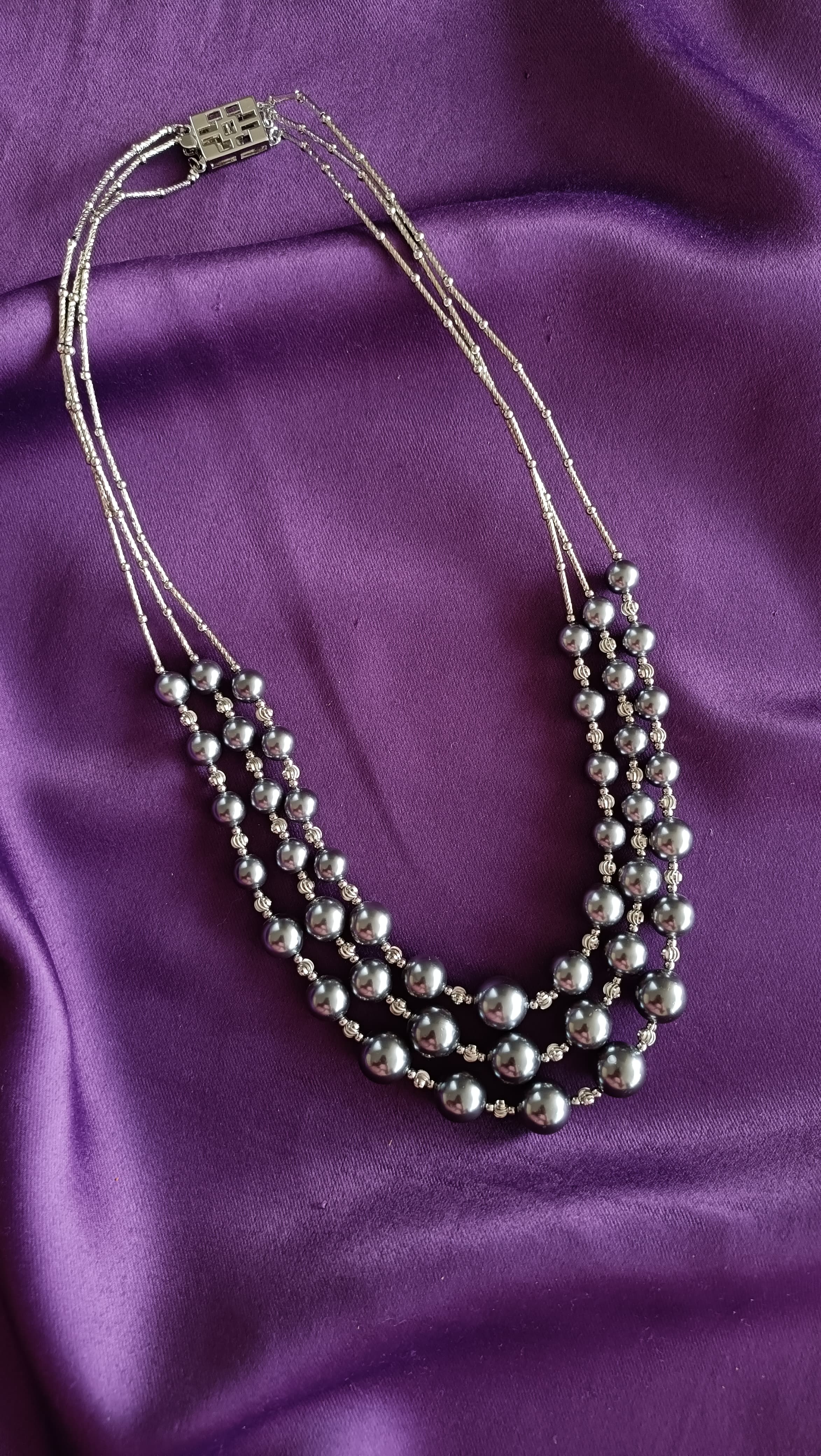 Silver Four-Strand Graduated Grey Pearl & Rondelle Spacer Necklace full length flat lay on purple fabric showing box clasp