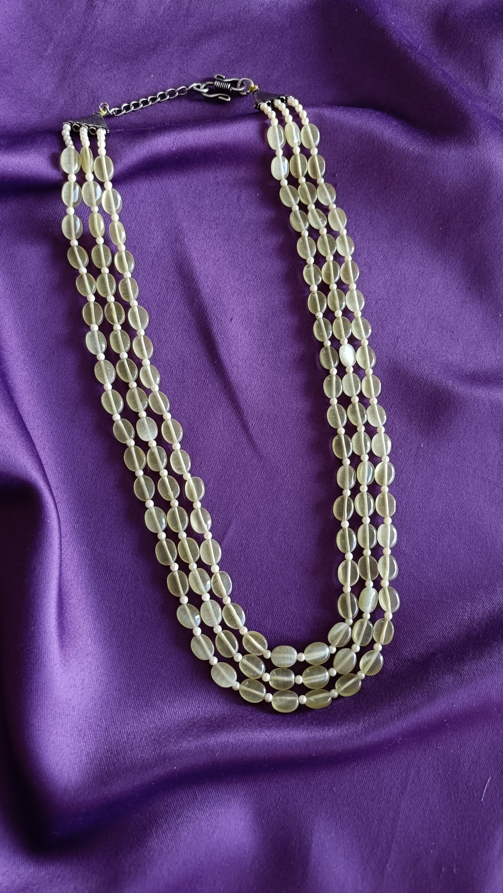 Triple-Strand Prehnite Green Tumbled Bead Necklace flat lay on purple fabric