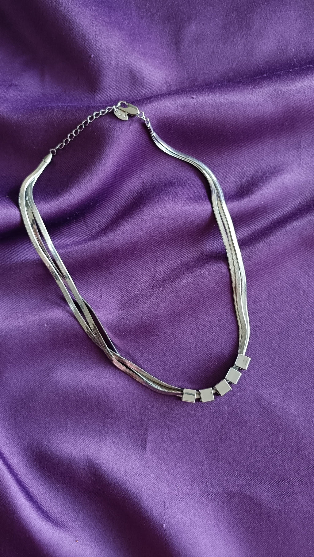 Silver Multi-Strand Herringbone Chain Necklace with Cube Bead Accents flat lay on purple fabric