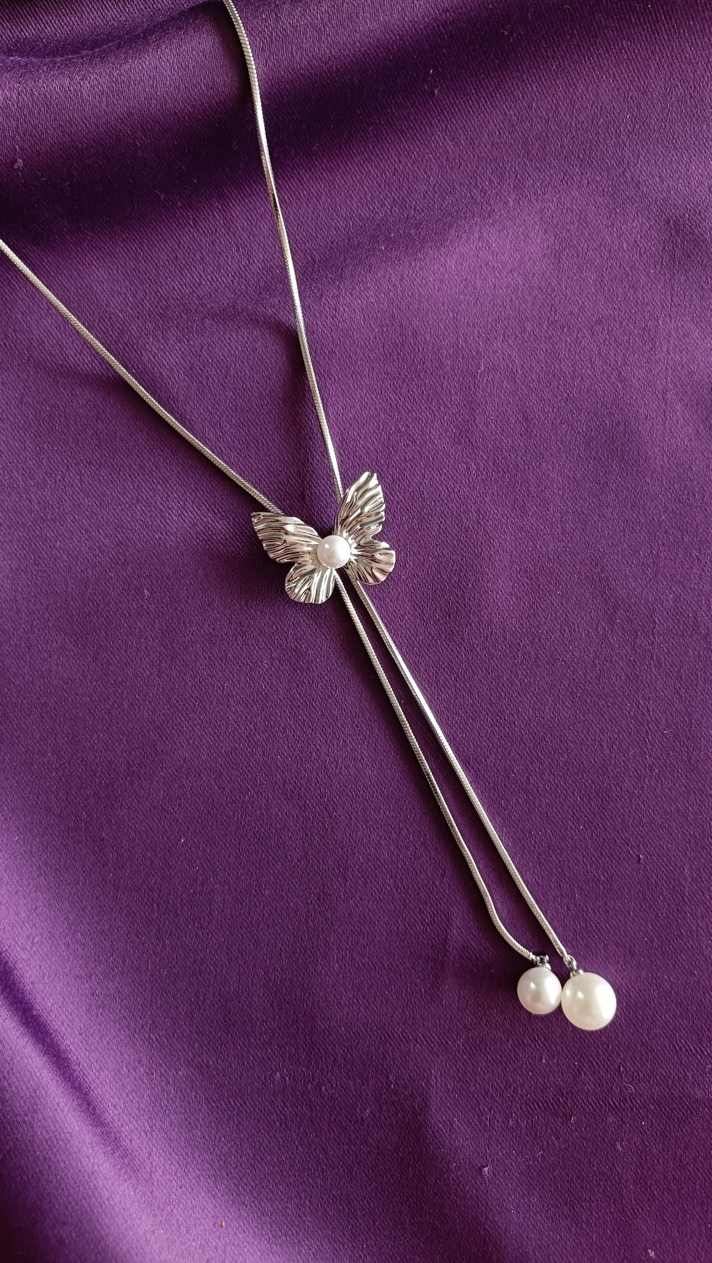 Silver Textured Butterfly Lariat Necklace with Double Pearl Drop detail flat lay on purple fabric