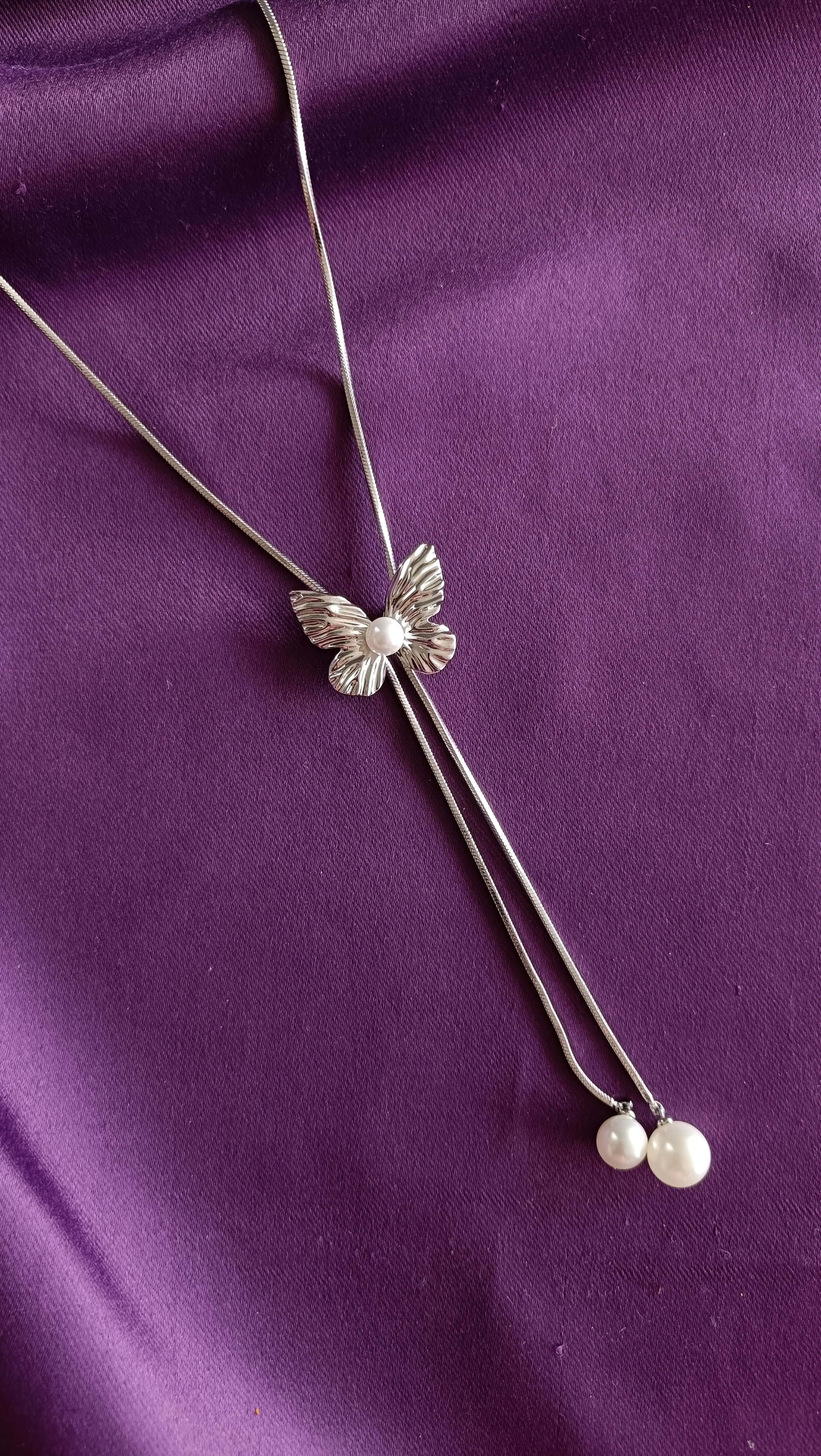 Silver Textured Butterfly Lariat Necklace with Double Pearl Drop detail flat lay on purple fabric