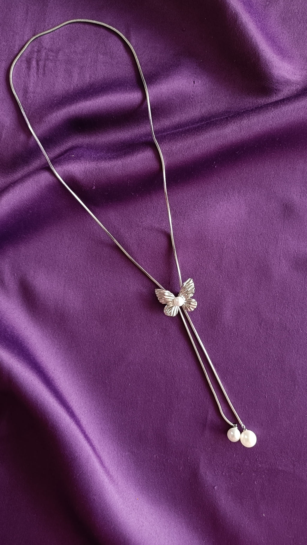 Silver Textured Butterfly Lariat Necklace with Double Pearl Drop flat lay on purple fabric