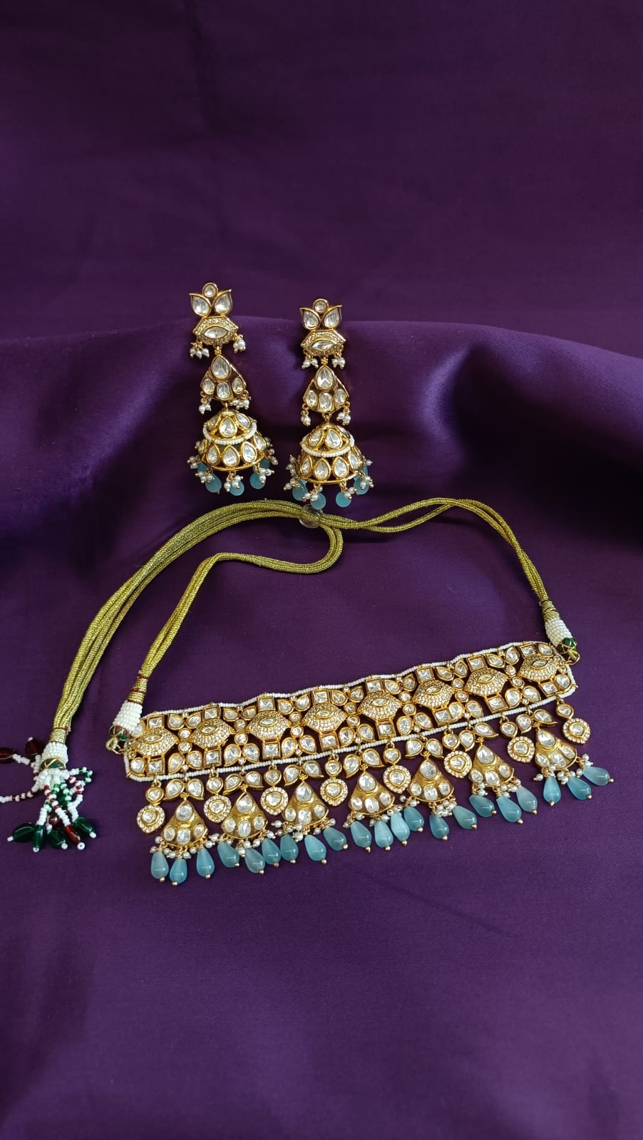 Gold Kundan Polki Wide Choker & Three-Tier Jhumka Earrings Set full flat lay on purple fabric showing dori cord and tassel