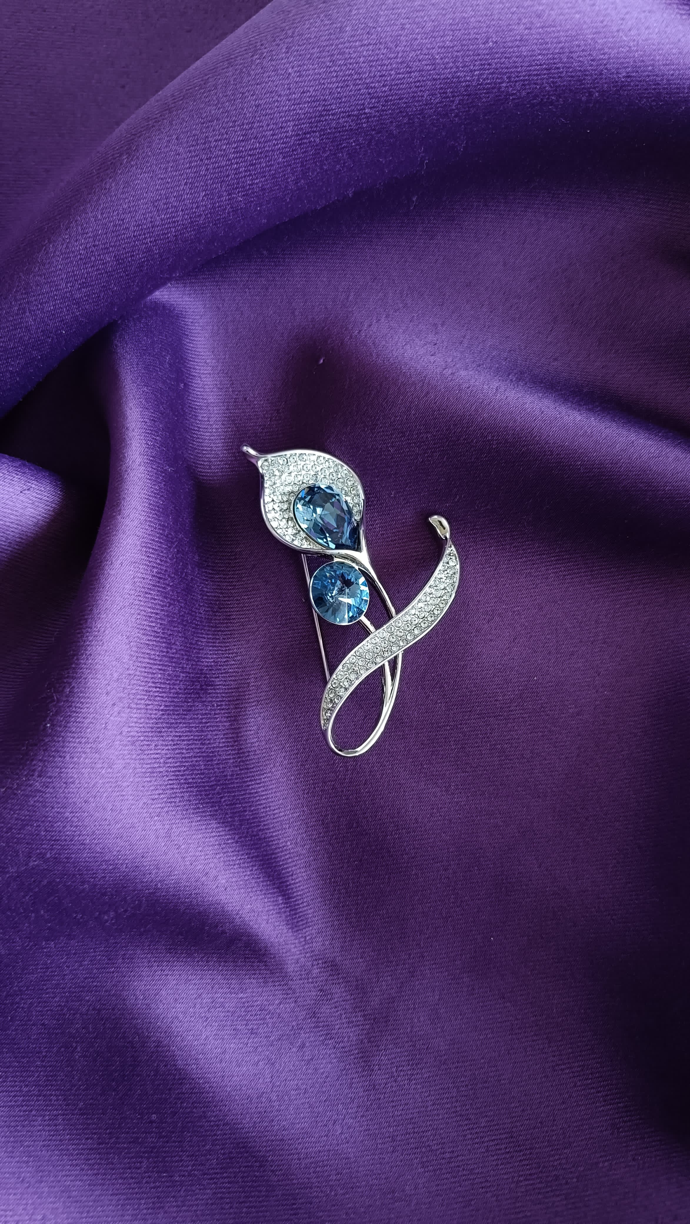 Silver Blue Topaz Crystal & Pavé Double Bloom Lapel Brooch Pin front view flat lay on purple fabric showing blue topaz crystals and pavé ribbon curl stem