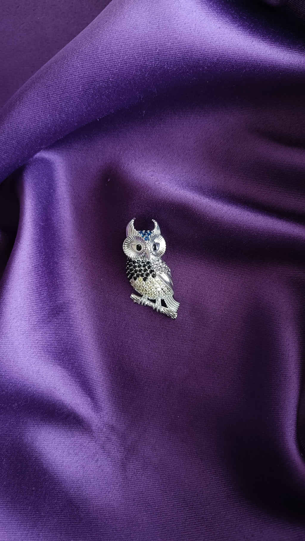 Silver Black & White Pavé Owl Lapel Brooch Pin front view flat lay on purple fabric showing white & black pavé detail, teal ear tufts and black crystal eyes