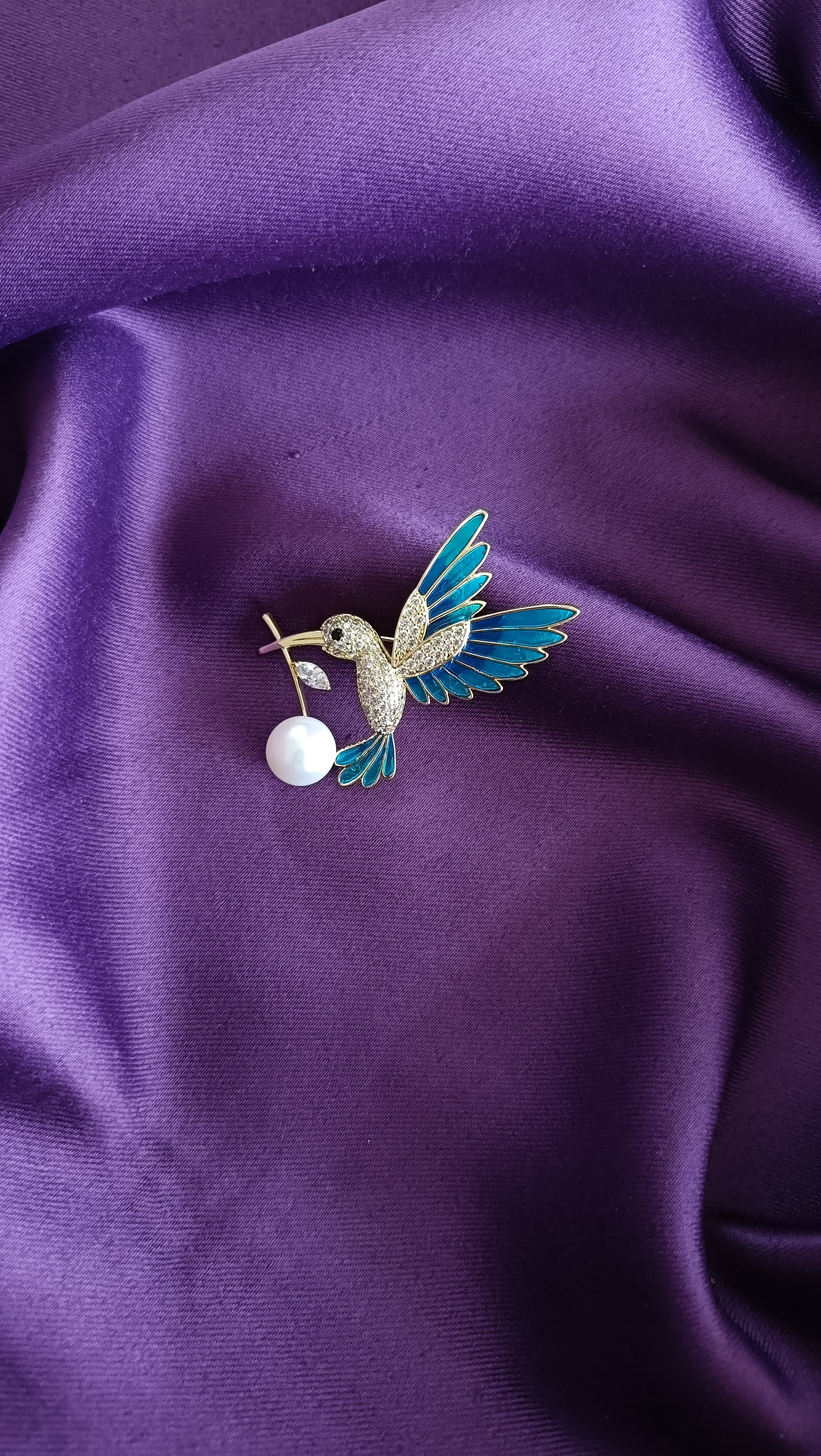 Gold Teal Enamel Hummingbird Pavé Body Lapel Brooch Pin with Pearl Drop front view flat lay on purple fabric showing teal enamel wings, pavé body and pearl drop