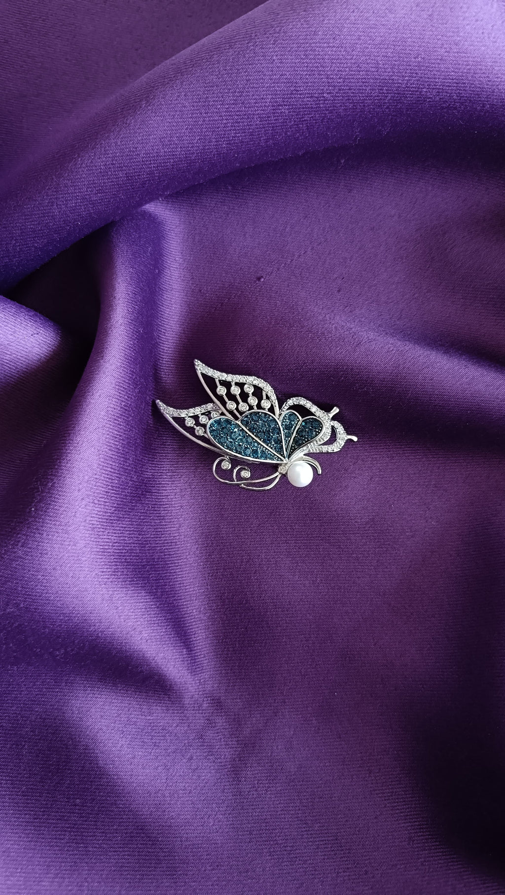 Silver Teal Pavé & White Crystal Butterfly Lapel Brooch Pin with Pearl Body front view flat lay on purple fabric showing teal pavé upper wing, white scalloped border and pearl body