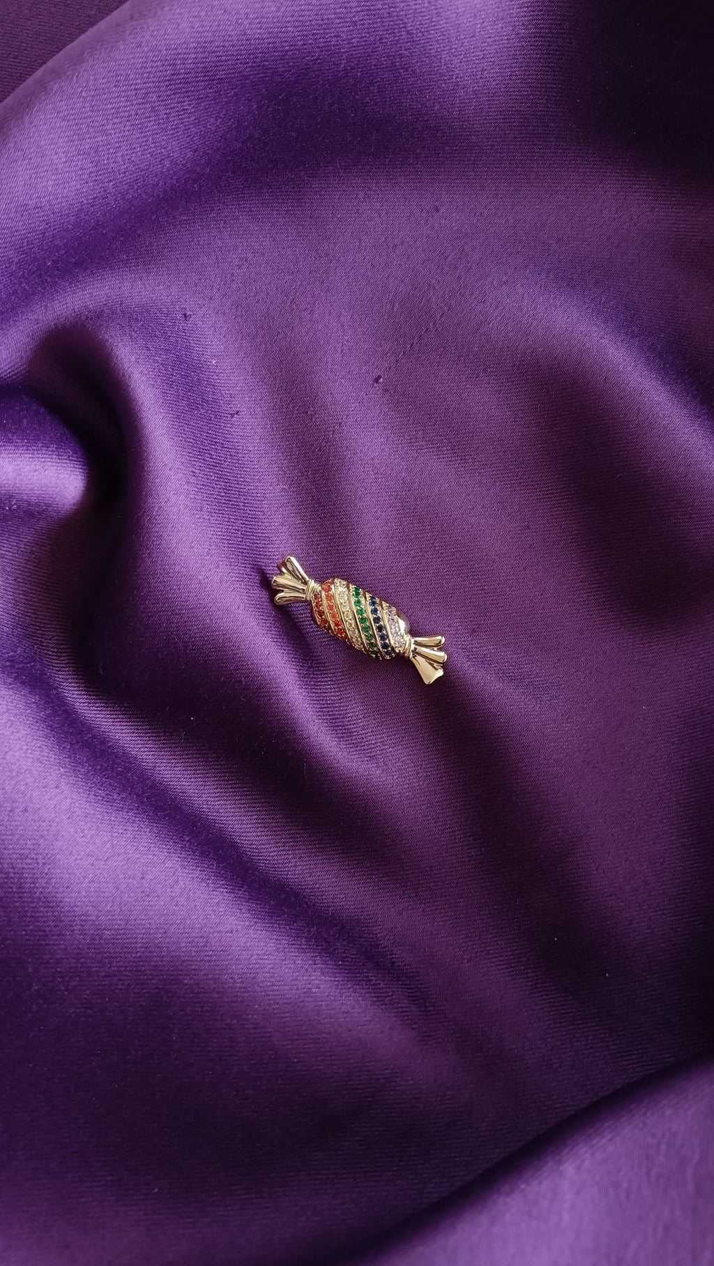 Gold Multicolour Pavé Candy Sweet Lapel Brooch Pin front view flat lay on purple fabric showing red, green, blue and white pavé crystal stripes and gold wrapper ends