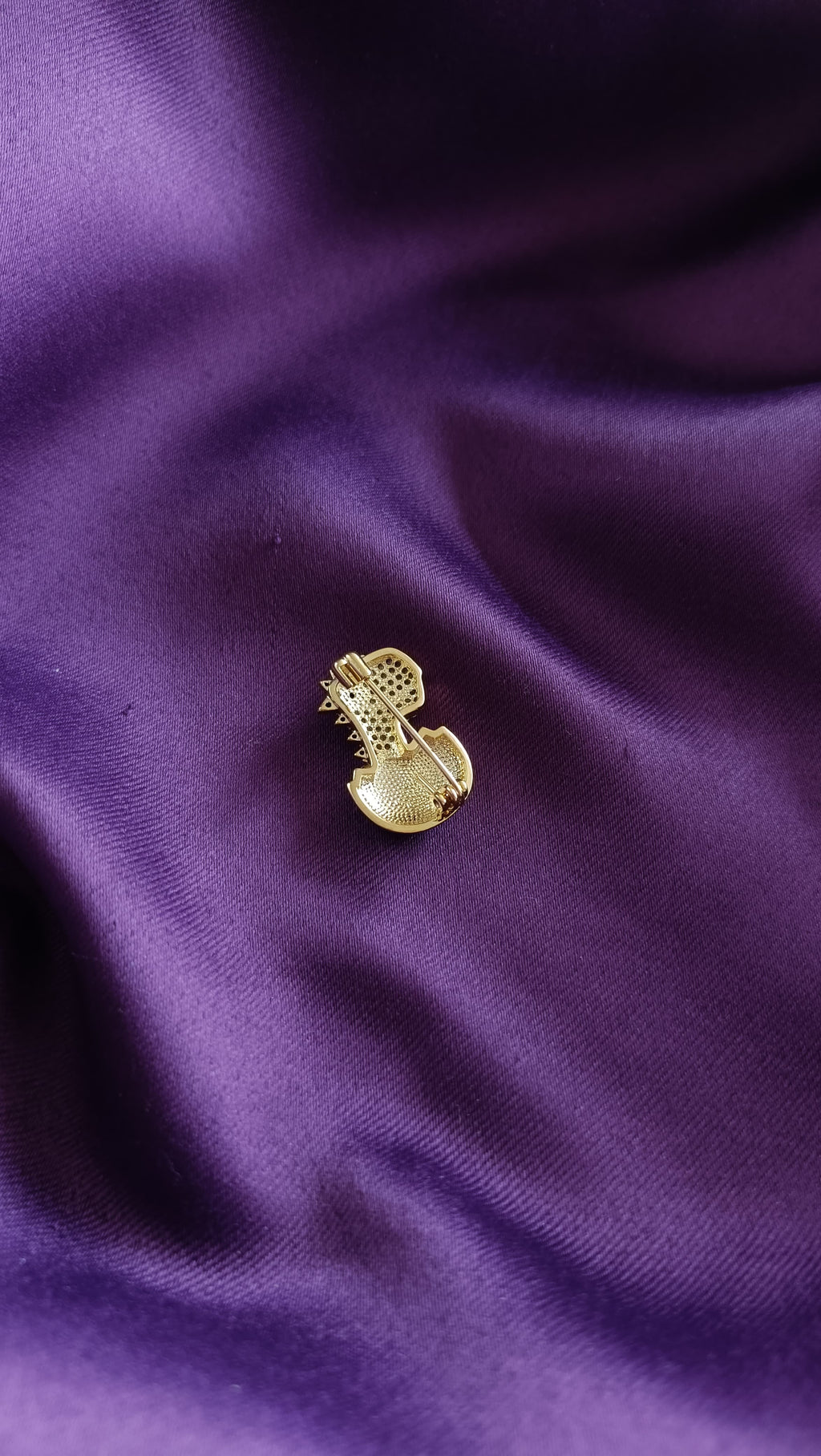 Gold Pavé Baby Dinosaur Hatching from Egg Lapel Brooch Pin reverse side flat lay on purple fabric showing gold egg body and pin back closure