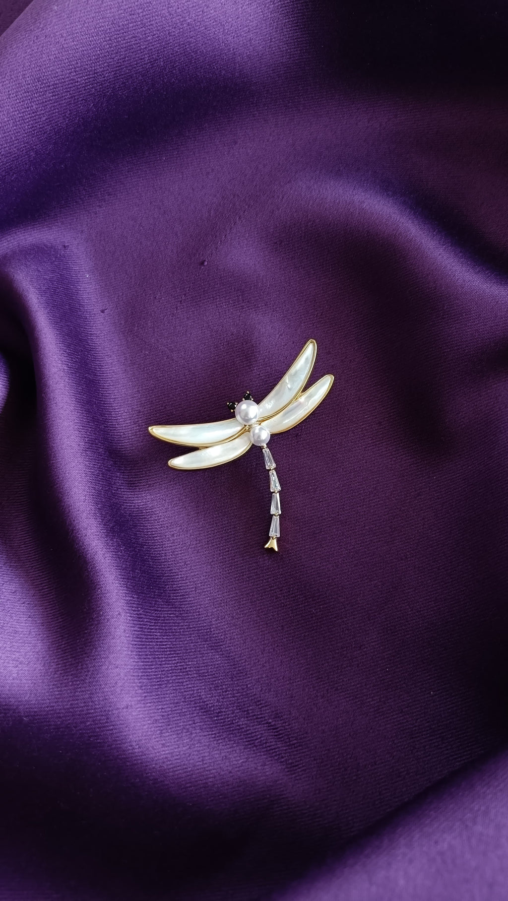 Gold Mother-of-Pearl Wing Dragonfly & Pearl Body Lapel Brooch Pin front view flat lay on purple fabric showing MOP wings, pearl body and baguette crystal tail