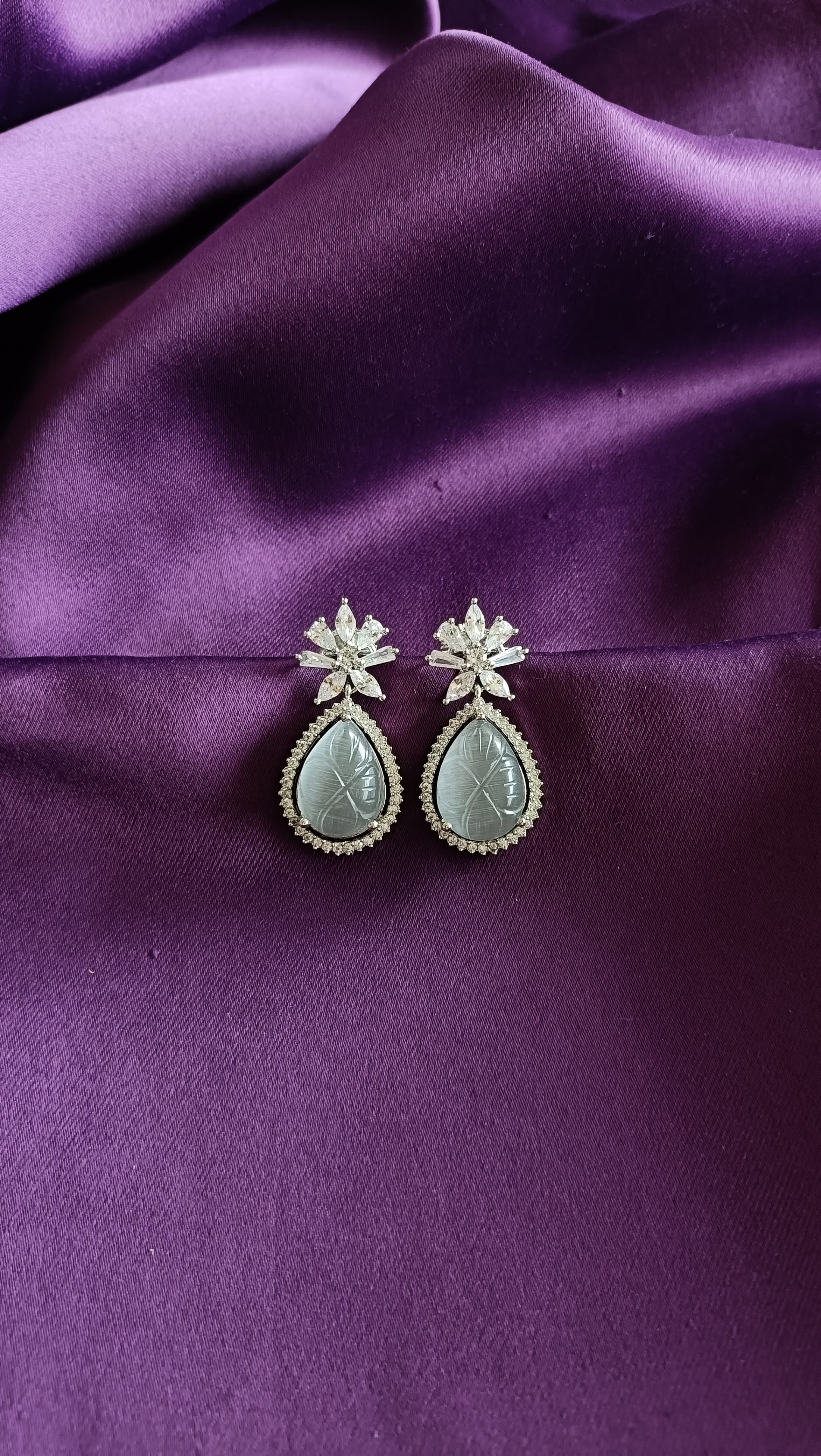 Silver Carved Jade Pear-Drop & Marquise Crystal Flower Drop Earrings close-up flat lay on purple fabric