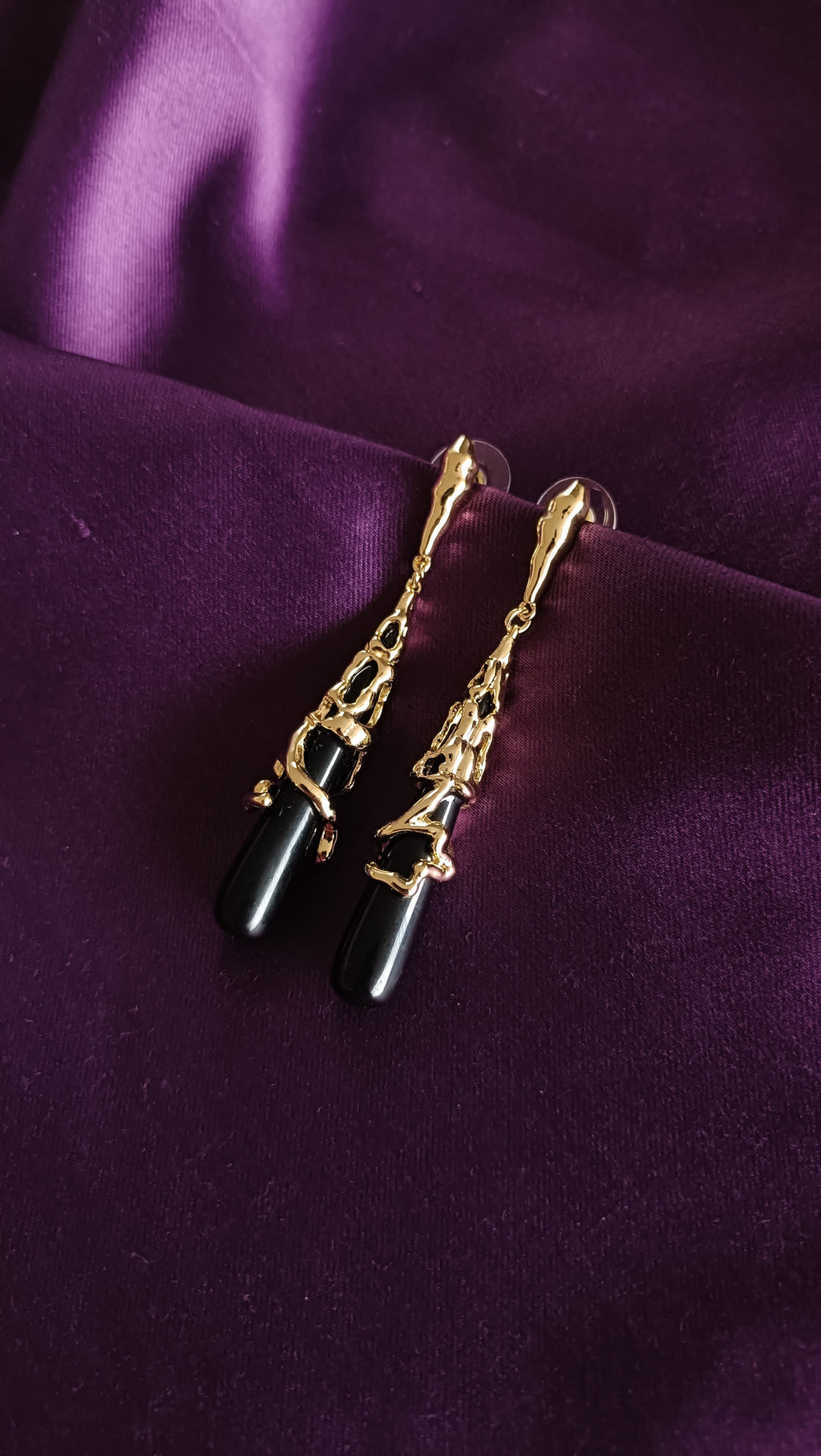 Gold Molten Sculptural Black Onyx Drop Earrings angled flat lay on purple fabric