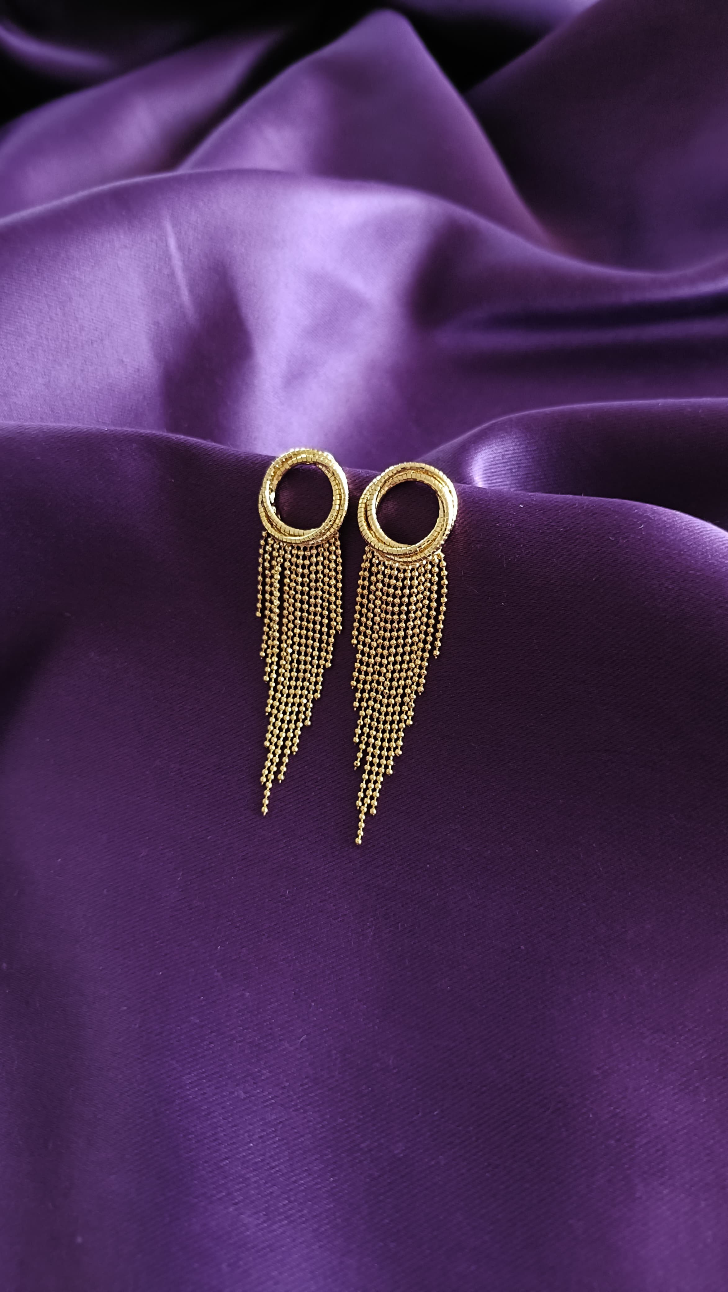 Gold Textured Open Circle Ball Chain Fringe Tassel Earrings pair angled flat lay on purple fabric