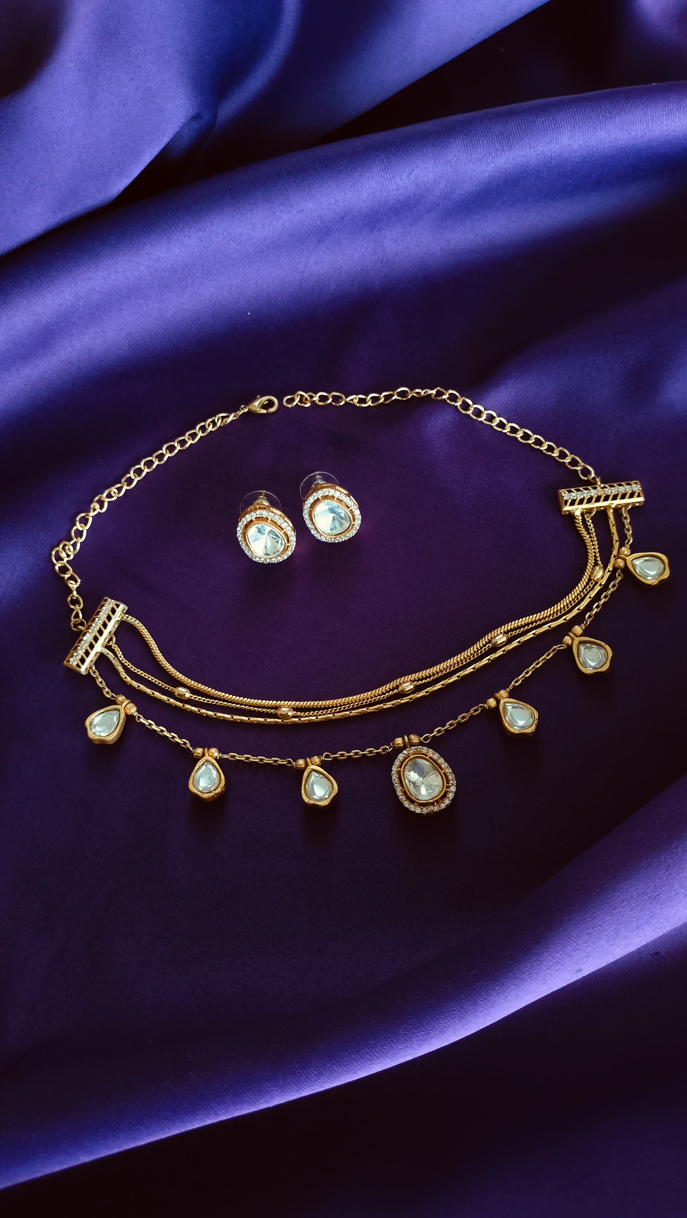 Gold Triple-Strand Polki Pear-Drop Charm Necklace & Oval Polki Pavé Stud Earrings Set full flat lay on purple fabric