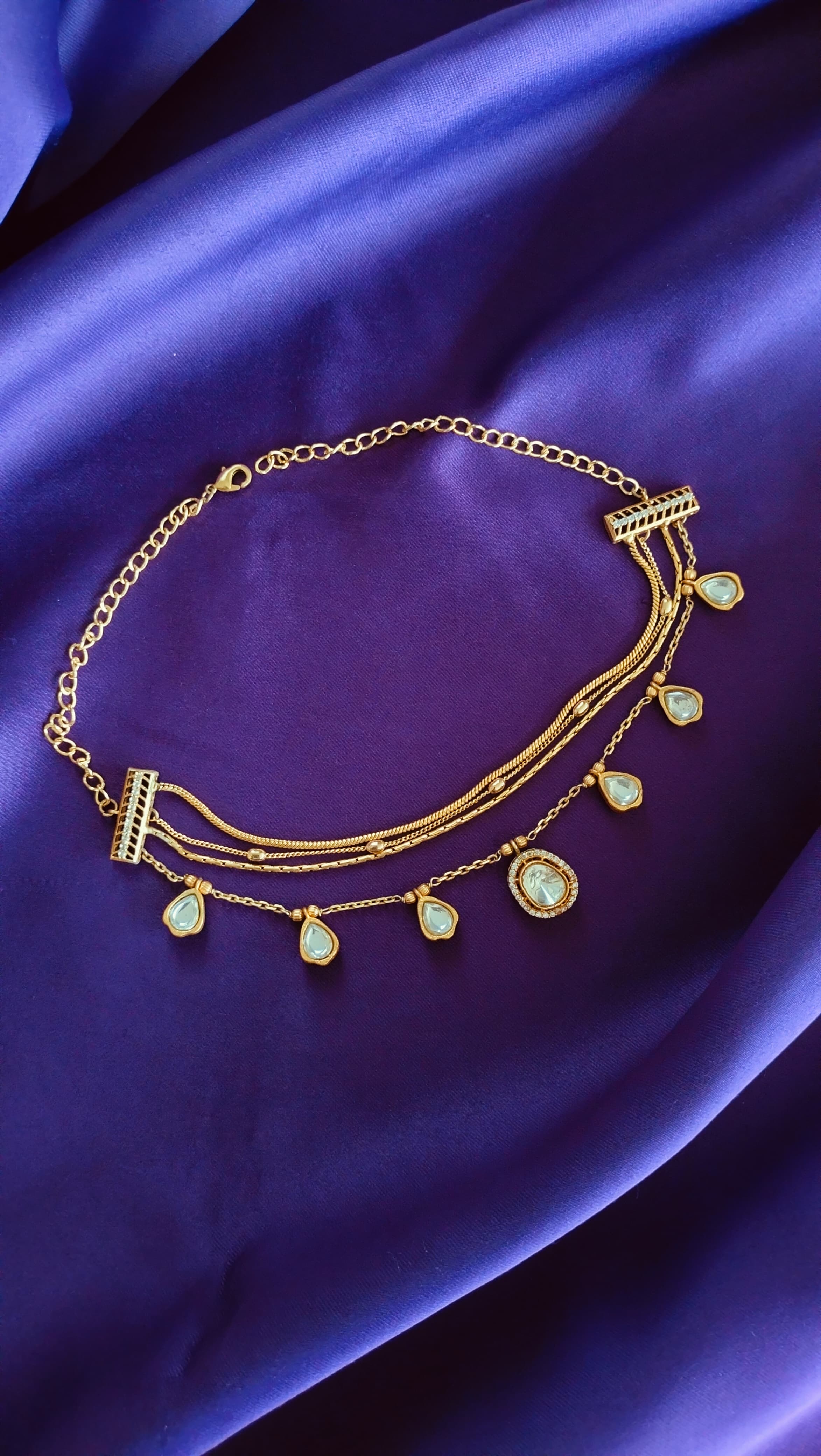 Gold Triple-Strand Polki Pear-Drop Charm Necklace full length flat lay on purple fabric showing ribbed bar clasps and lobster clasp extender