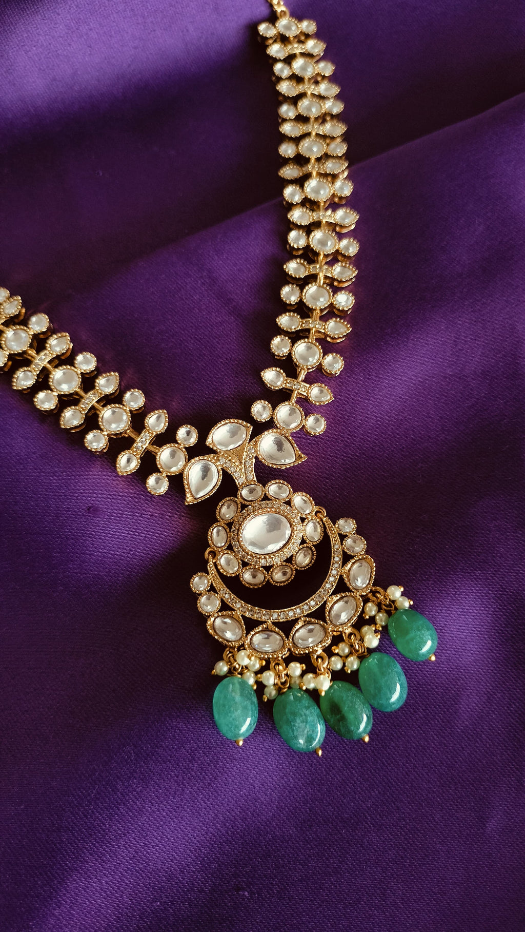 Gold Kundan Polki Graduated Necklace with Chandbali Pendant flat lay on purple fabric
